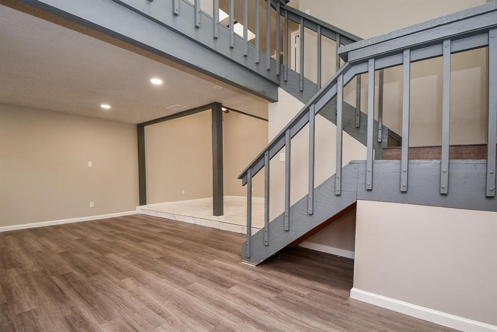 This photo showcases a modern interior with laminate wood flooring, a two-tone staircase with gray railings, and recessed lighting, offering a spacious and open feel.