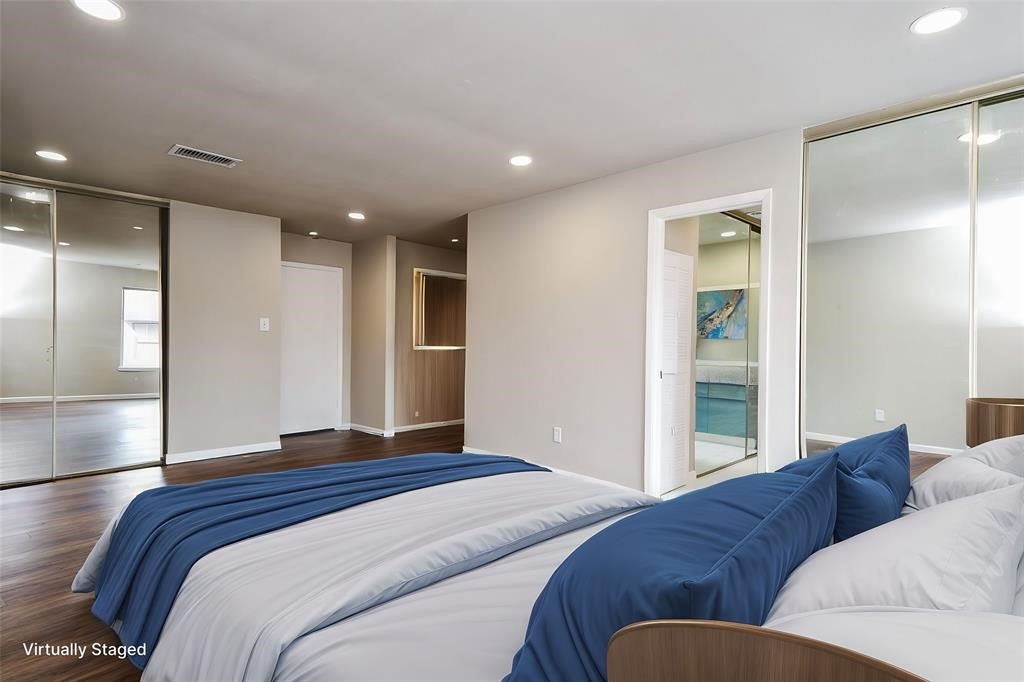 This virtually staged bedroom features a spacious layout with hardwood floors, recessed lighting, and mirrored closet doors. The neutral walls provide a fresh feel, and an ensuite bathroom offers added convenience. Virtual staging was used.