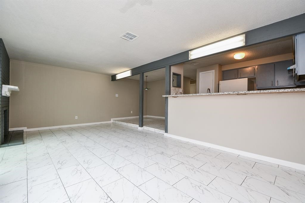 Spacious living area with modern tiled flooring, open layout, and a raised kitchen bar. The room features neutral tones and a cozy fireplace, creating an inviting atmosphere.