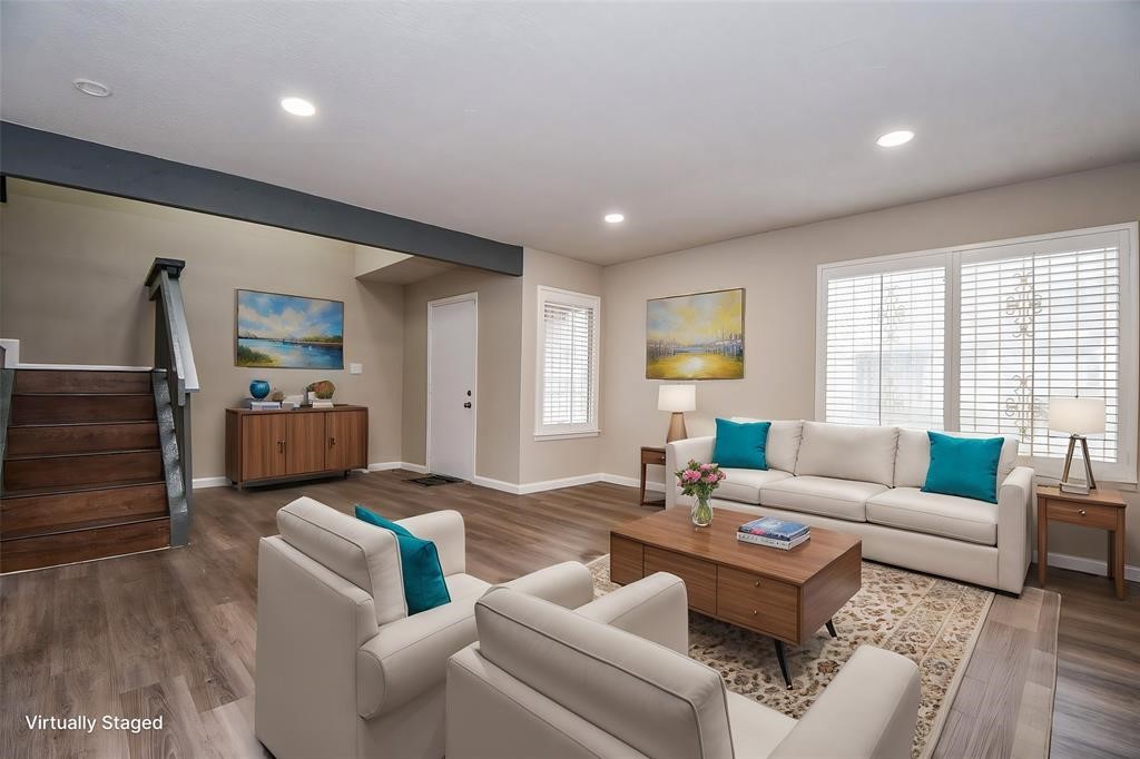 This photo showcases a bright, modern living room with hardwood floors, stylish furniture, and large windows. The neutral walls complement the vibrant decor accents. A staircase adds architectural interest, and the space feels open and inviting.Virtual staging was used.