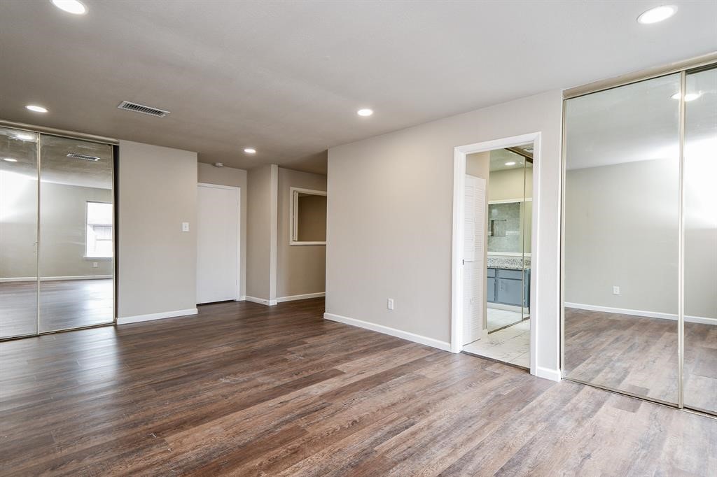 Spacious room with hardwood flooring, neutral walls, and recessed lighting. Features mirrored sliding closet doors and an attached bathroom, creating a modern, open feel.