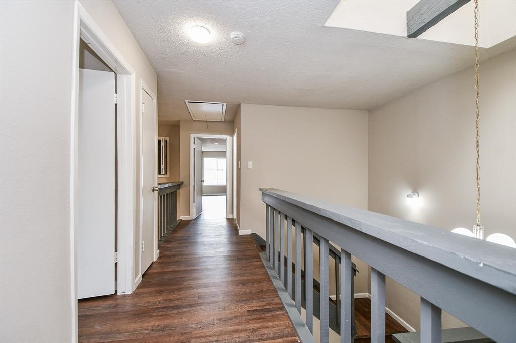 This photo shows a hallway with wood flooring, neutral walls, and a staircase railing. It leads to a bright room with a window at the end, offering a clean and open feel.