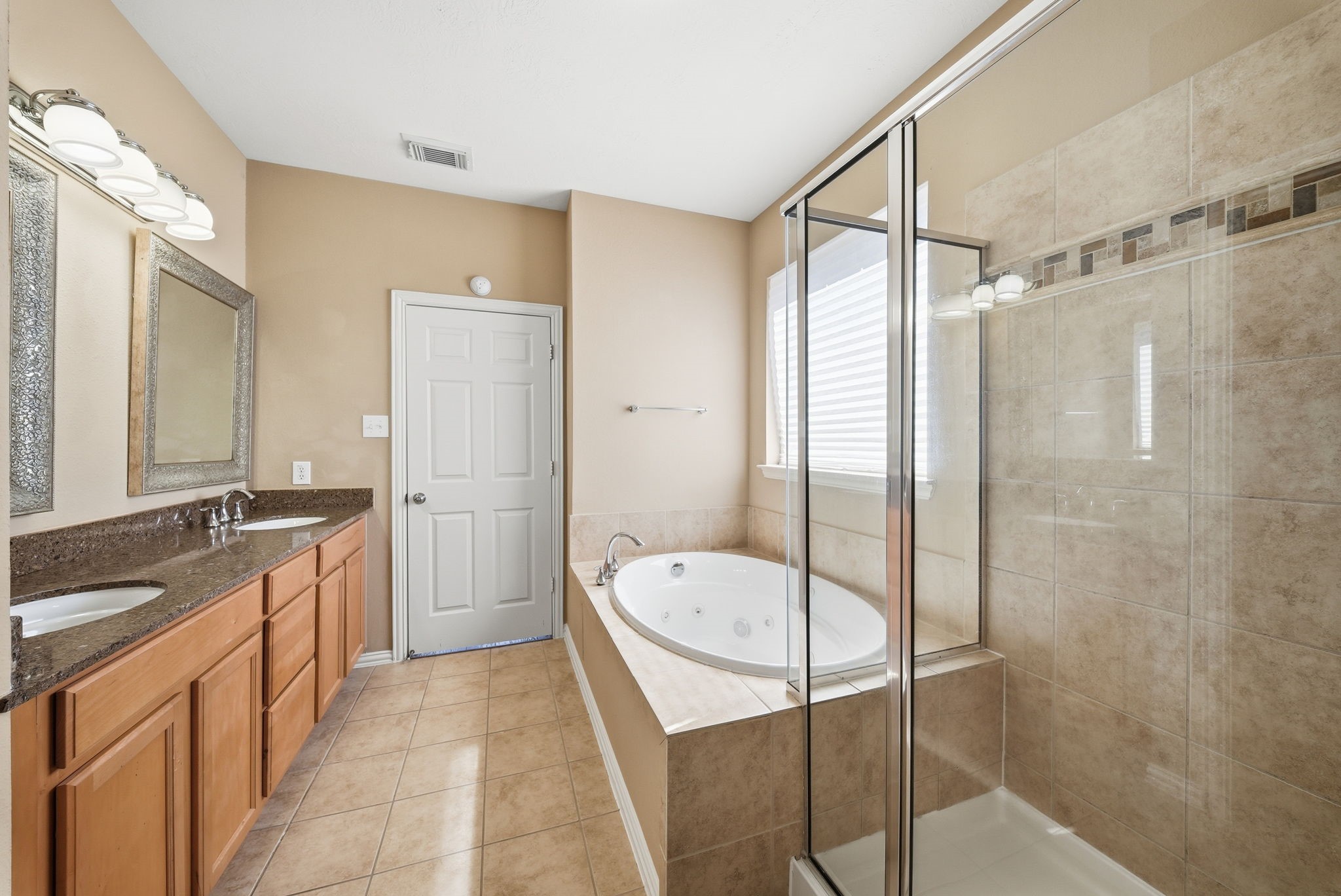 Unwind in the primary bathroom featuring a jetted tub, separate glass-enclosed shower, dual sinks, generous vanity storage, and a private enclosed toilet area.