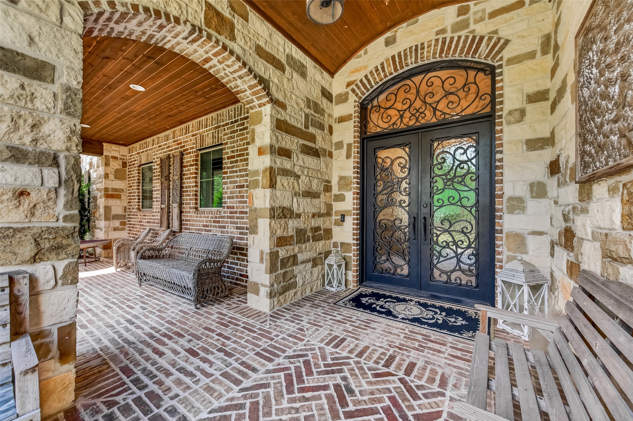 Covered front porch with stone arches, a stained tongue-and-groove ceiling and a herringbone brick floor. Arched wrought-iron double doors open to the foyer. Covered front porch with stone arches, a stained tongue-and-groove ceiling and a herringbone brick floor. Arched wrought-iron double doors open to the foyer.