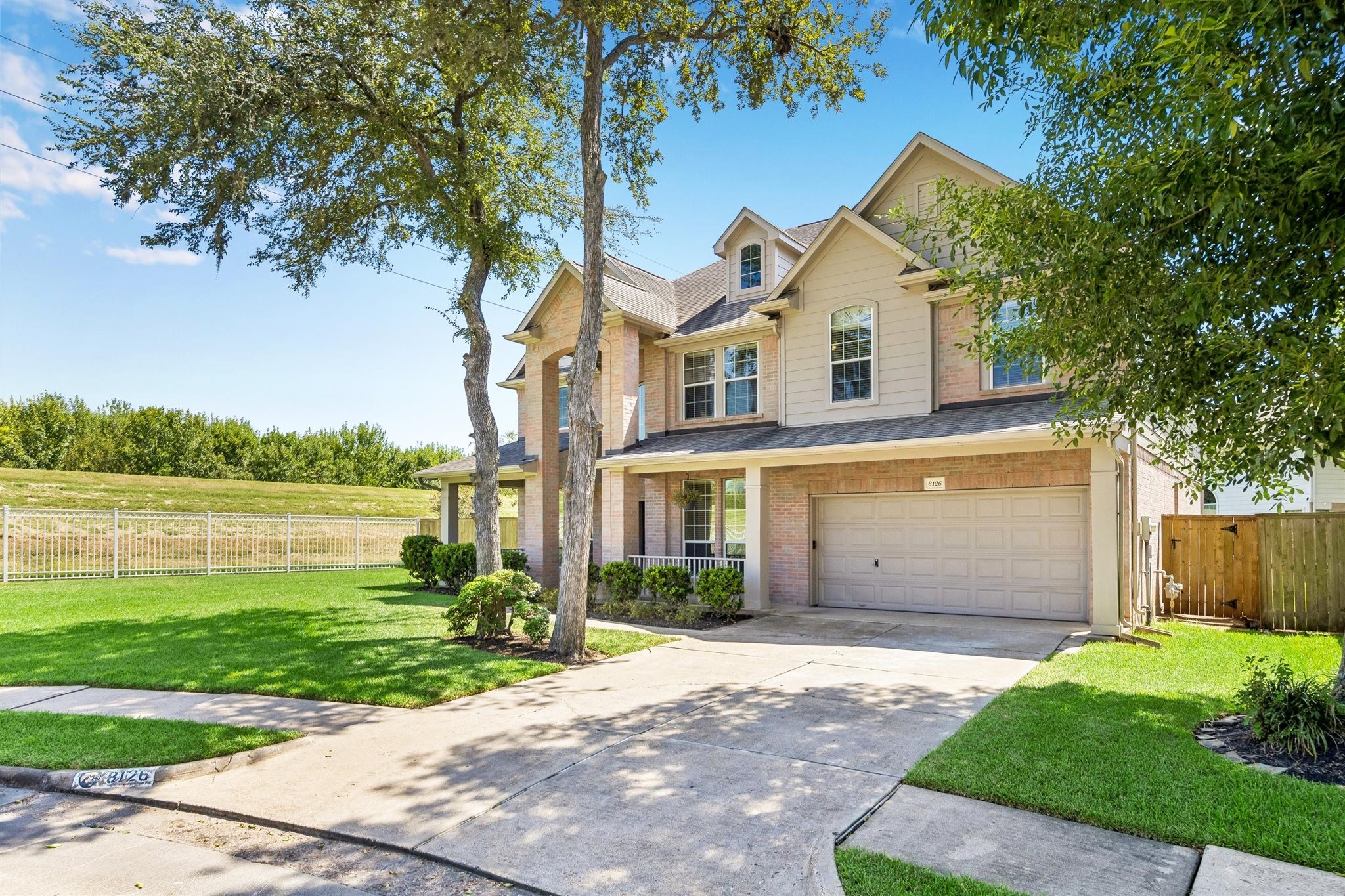 BEAUTIFUL FRONT ELEVATION SHOWCASING A SPACIOUS LAWN, MATURE TREES, AND AN OPEN GREENSPACE SETTING ALONG THE SIDE OF THE PROPERTY.