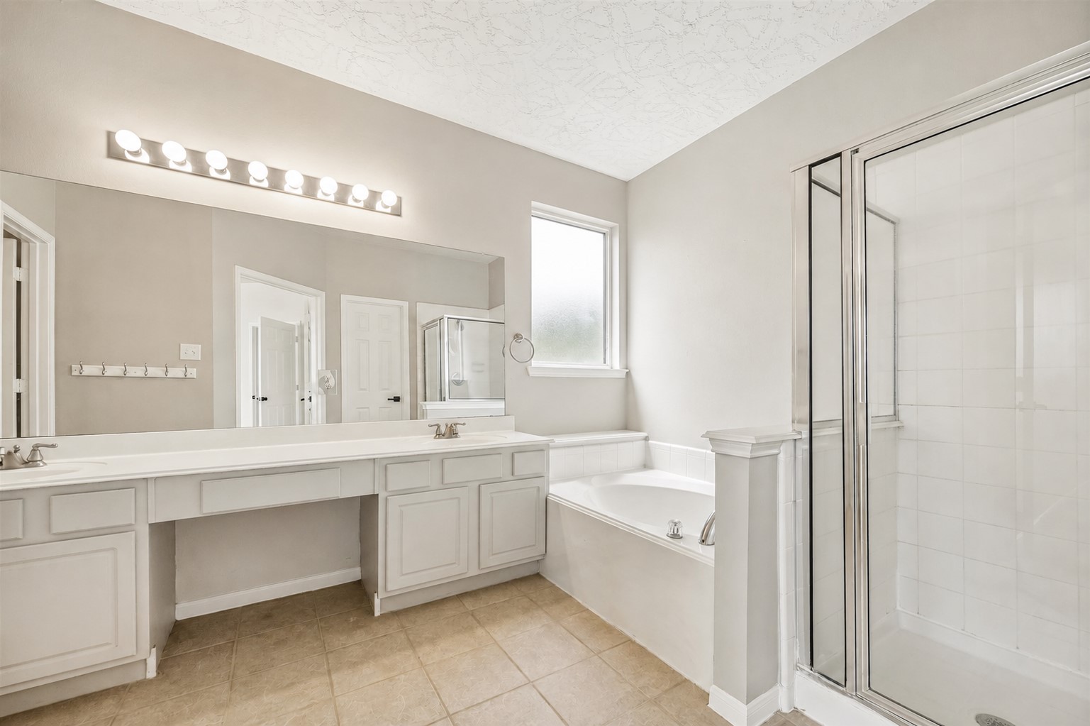PRIMARY BATH FEATURES AN EXTENDED VANITY, DEEP SOAKING TUB, AND SEPARATE GLASS-ENCLOSED SHOWER.