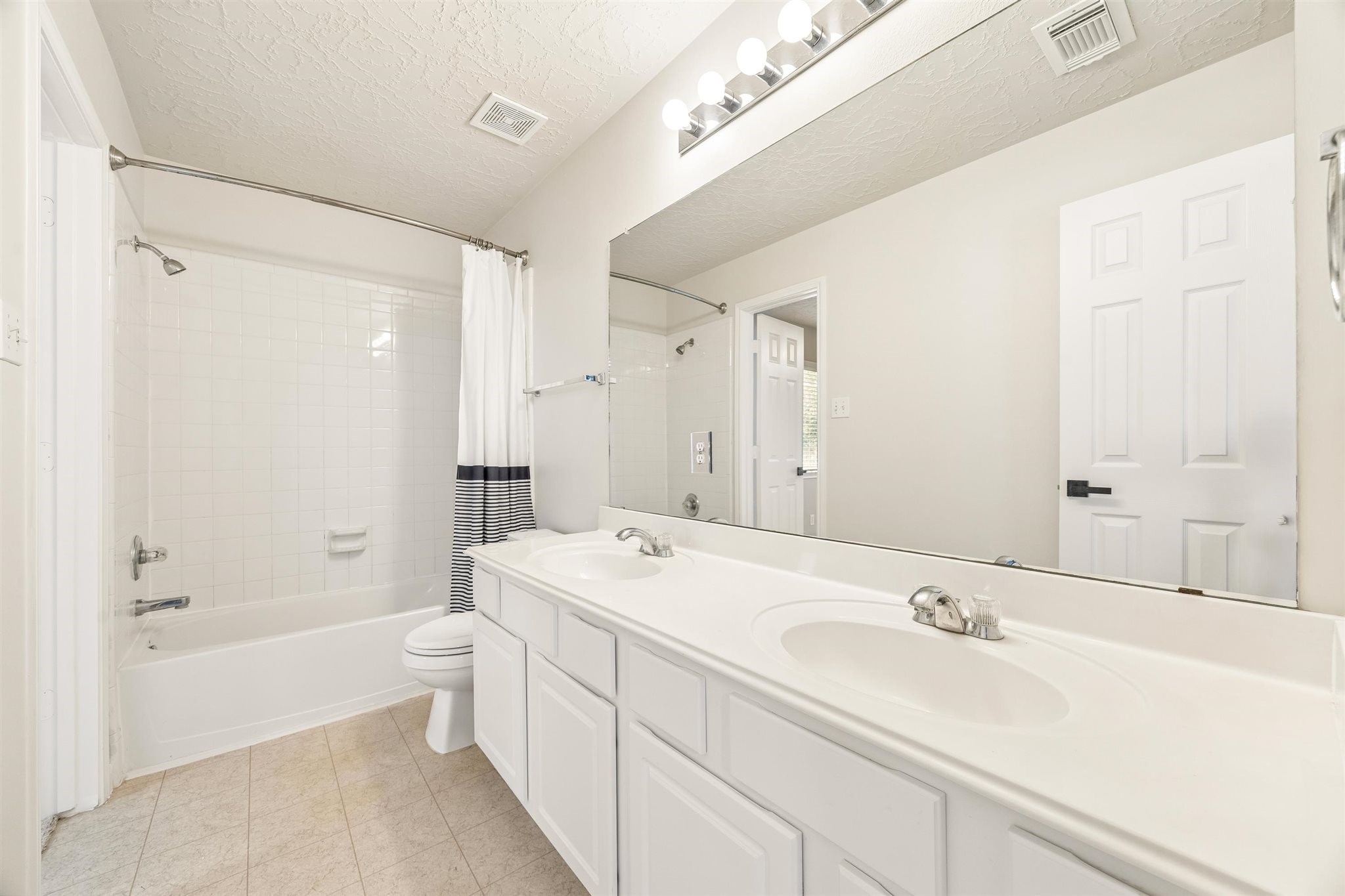 SECONDARY BATH FEATURES A DOUBLE-SINK VANITY, LARGE MIRROR, AND SEPARATE TUB AND SHOWER AREA.