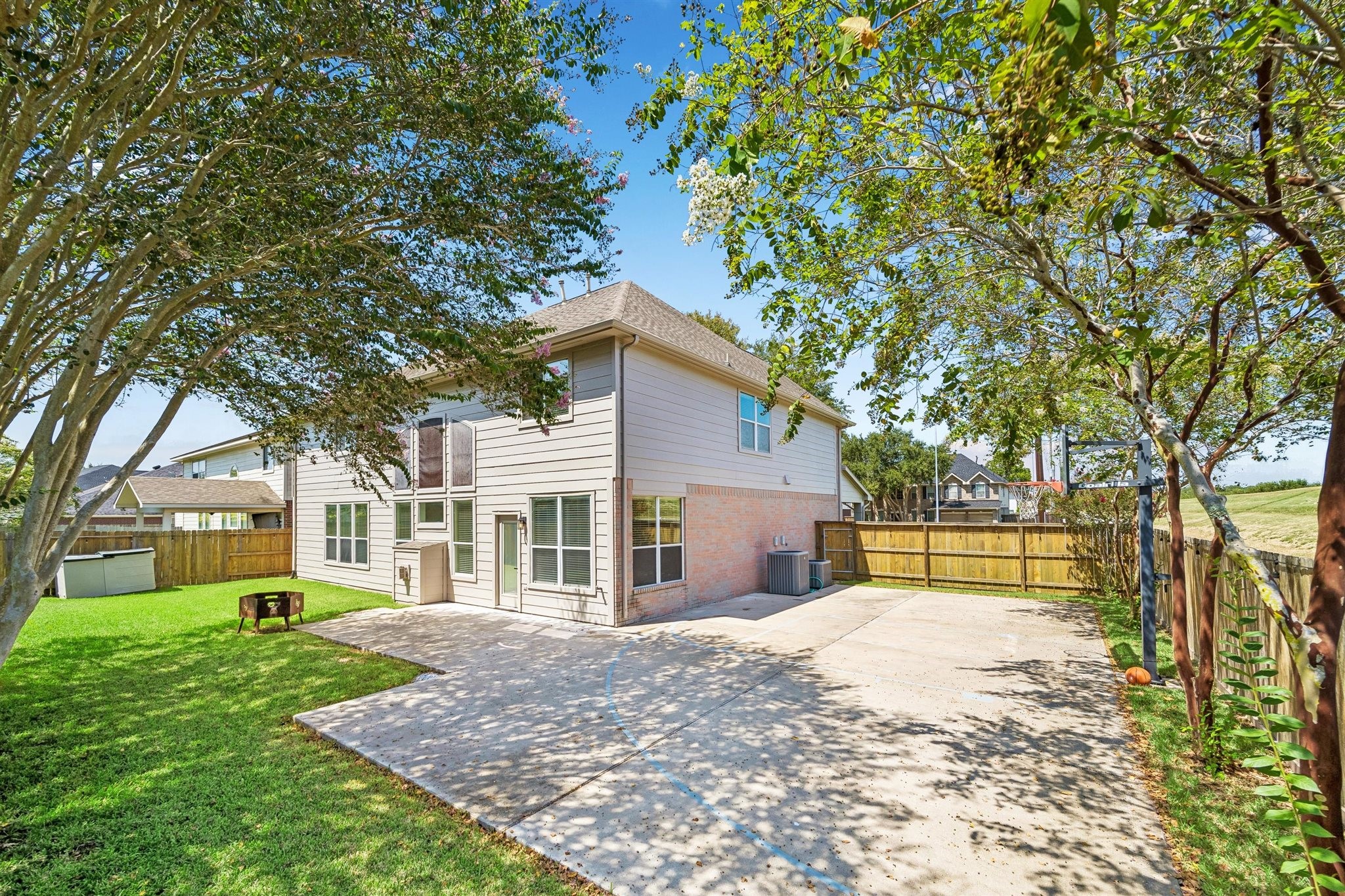 SPACIOUS BACKYARD WITH A LARGE CONCRETE PATIO, MATURE SHADE TREES, AND PLENTY OF OPEN LAWN.