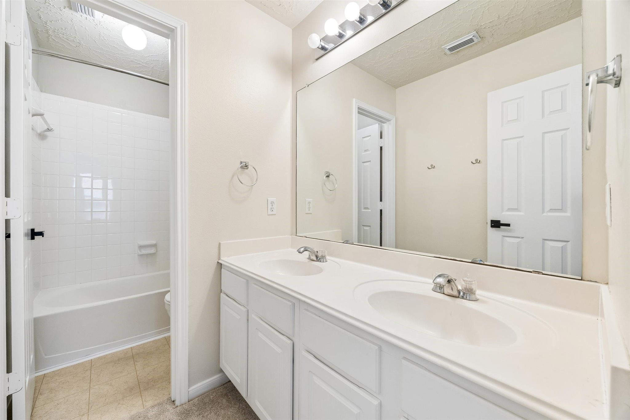 UPSTAIRS BATHROOM OFFERS A DOUBLE-SINK VANITY, EXPANSIVE MIRROR, AND TUB-SHOWER COMBINATION.