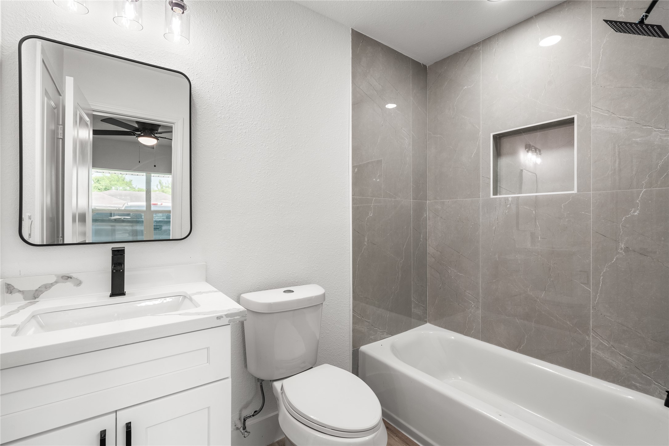 Elegant full bath boasting stylish matte black hardware, custom gray tile surround, and a pristine white vanityoffering a sophisticated, spa-like feel for guests and family alike.