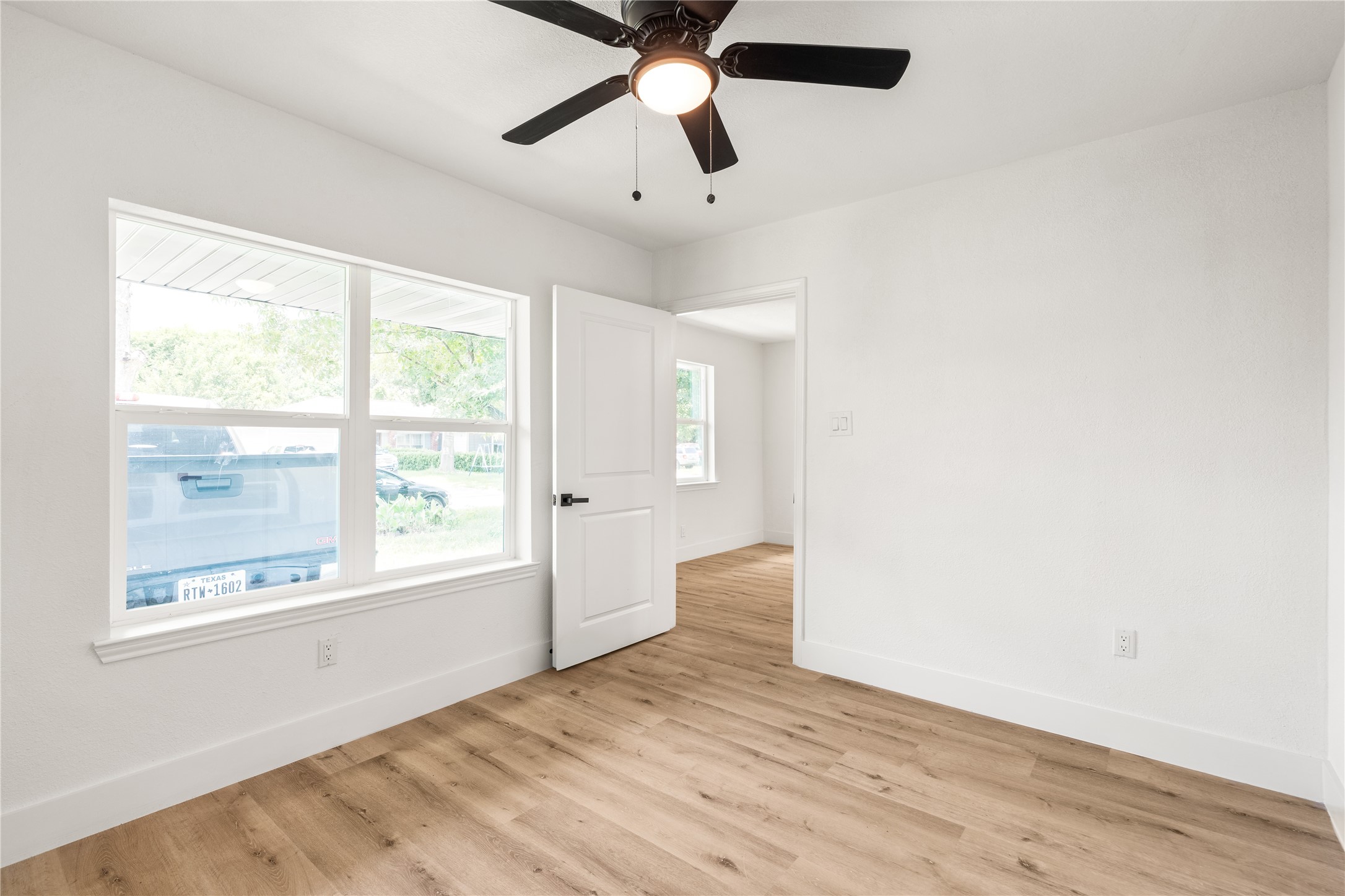 Light-filled primary bedroom featuring a double window, modern ceiling fan, warm wood-look flooring, and a crisp, seamless entry.