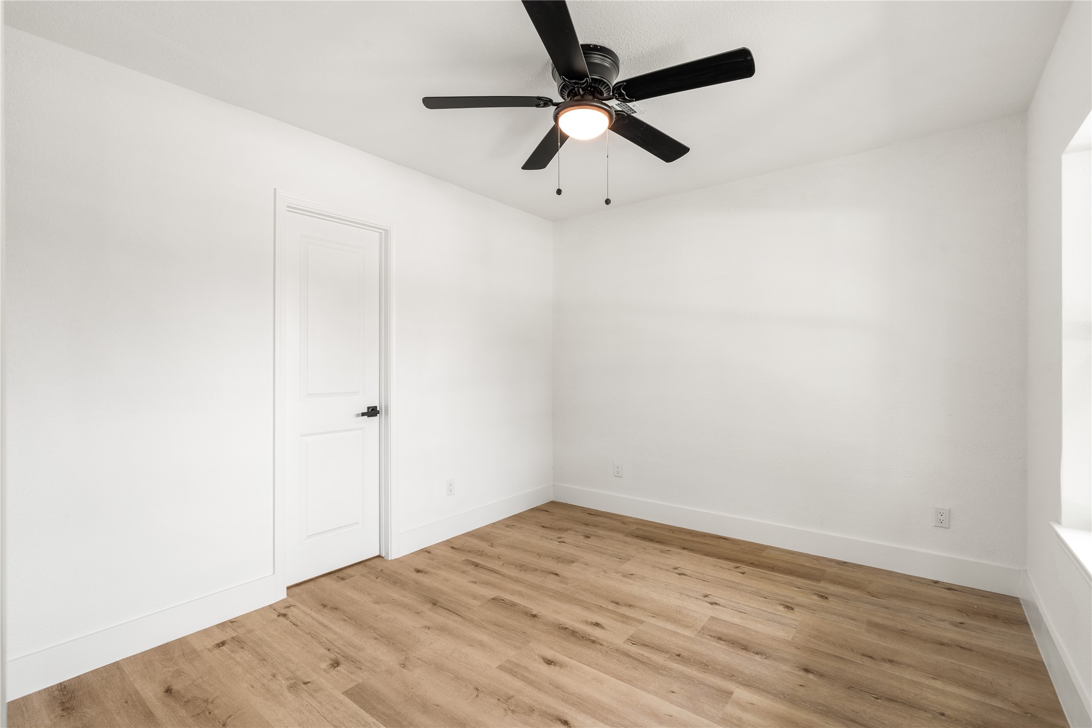 Reverse view of Bedroom showcasing warm wood-look flooring, crisp neutral walls, and a modern ceiling fan.