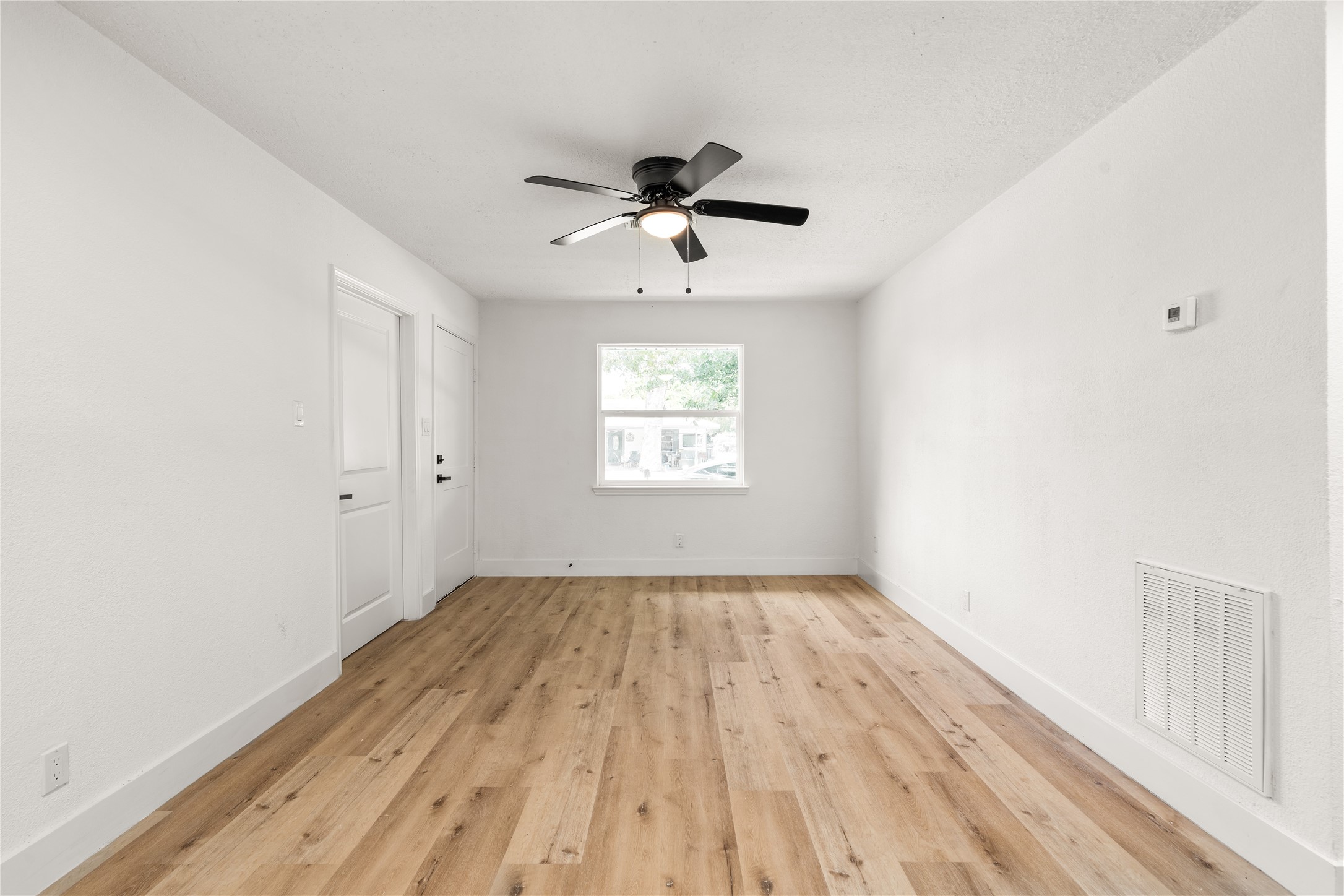 Living Area: Centered perspective highlighting rich wood-grain floors, fresh neutral finishes, efficient central HVAC features, and a bright focal window framing front-yard views. Living Area: Centered perspective highlighting rich wood-grain floors, fresh neutral finishes, efficient central HVAC features, and a bright focal window framing front-yard views.