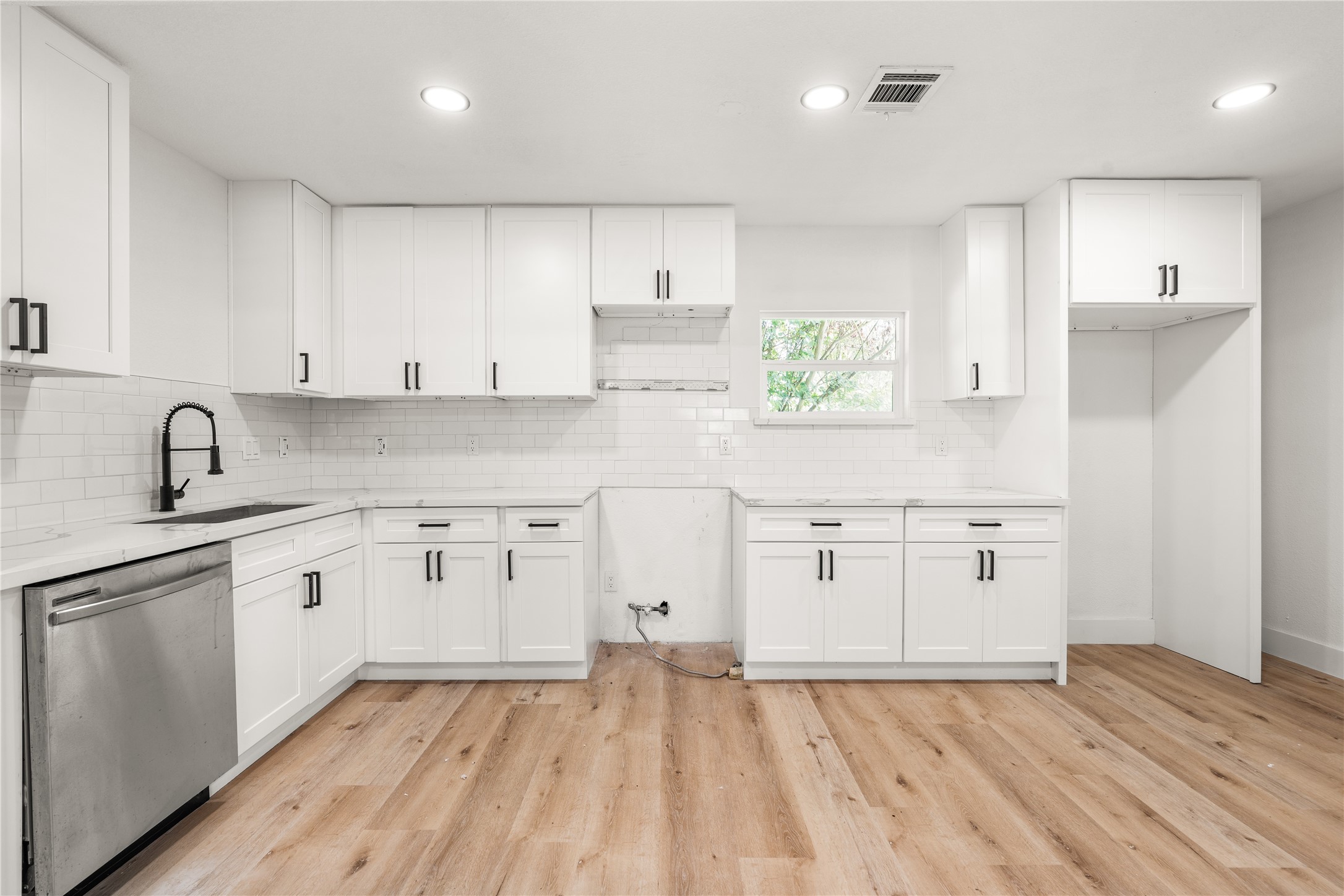 Modern kitchen showcasing sleek white shaker cabinets, classic subway tile, matte black accents, and rich wood-grain flooring.