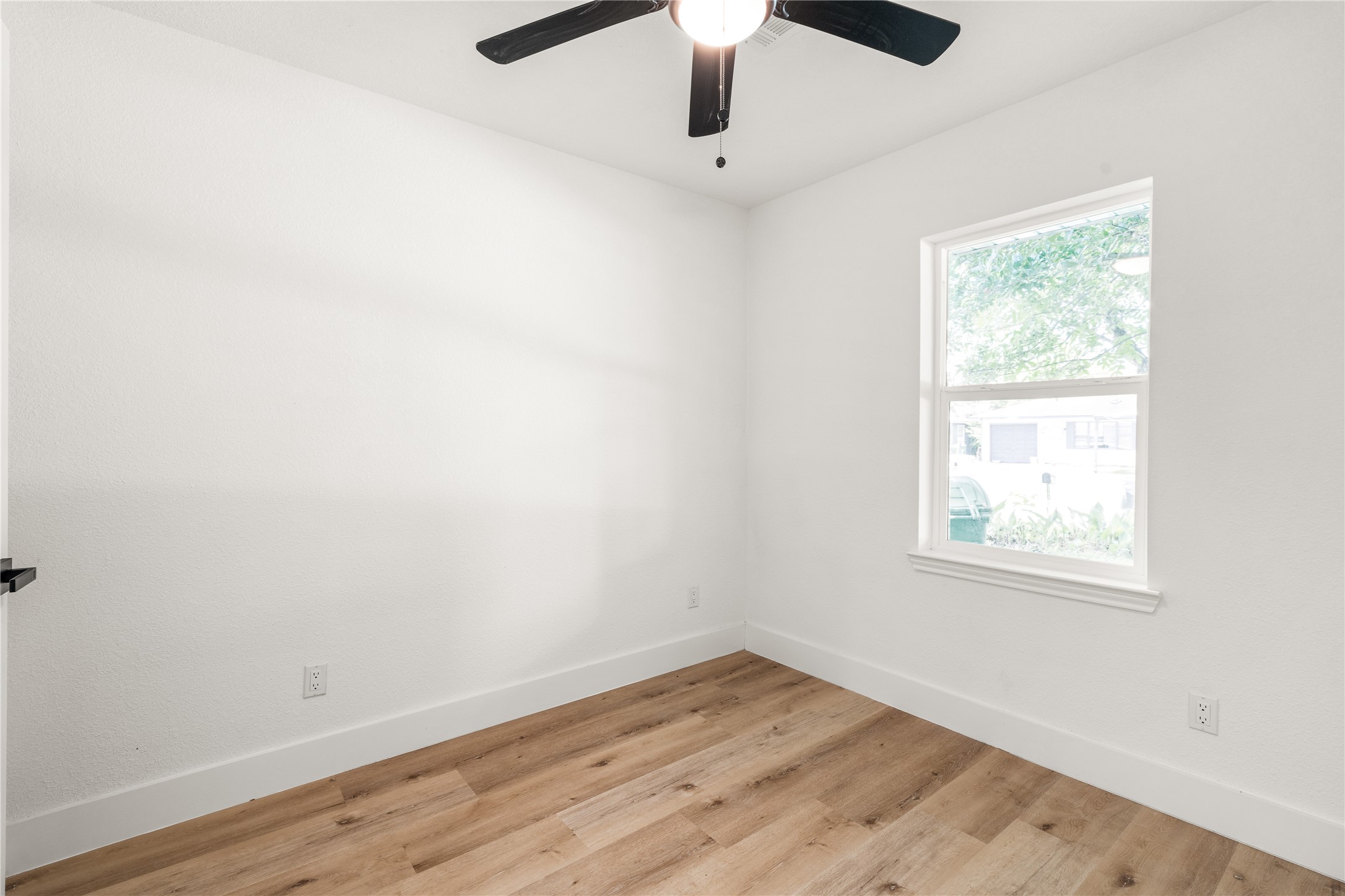 Bright secondary bedroom showcasing crisp neutral walls, warm wood-grain flooring, and lovely natural light.