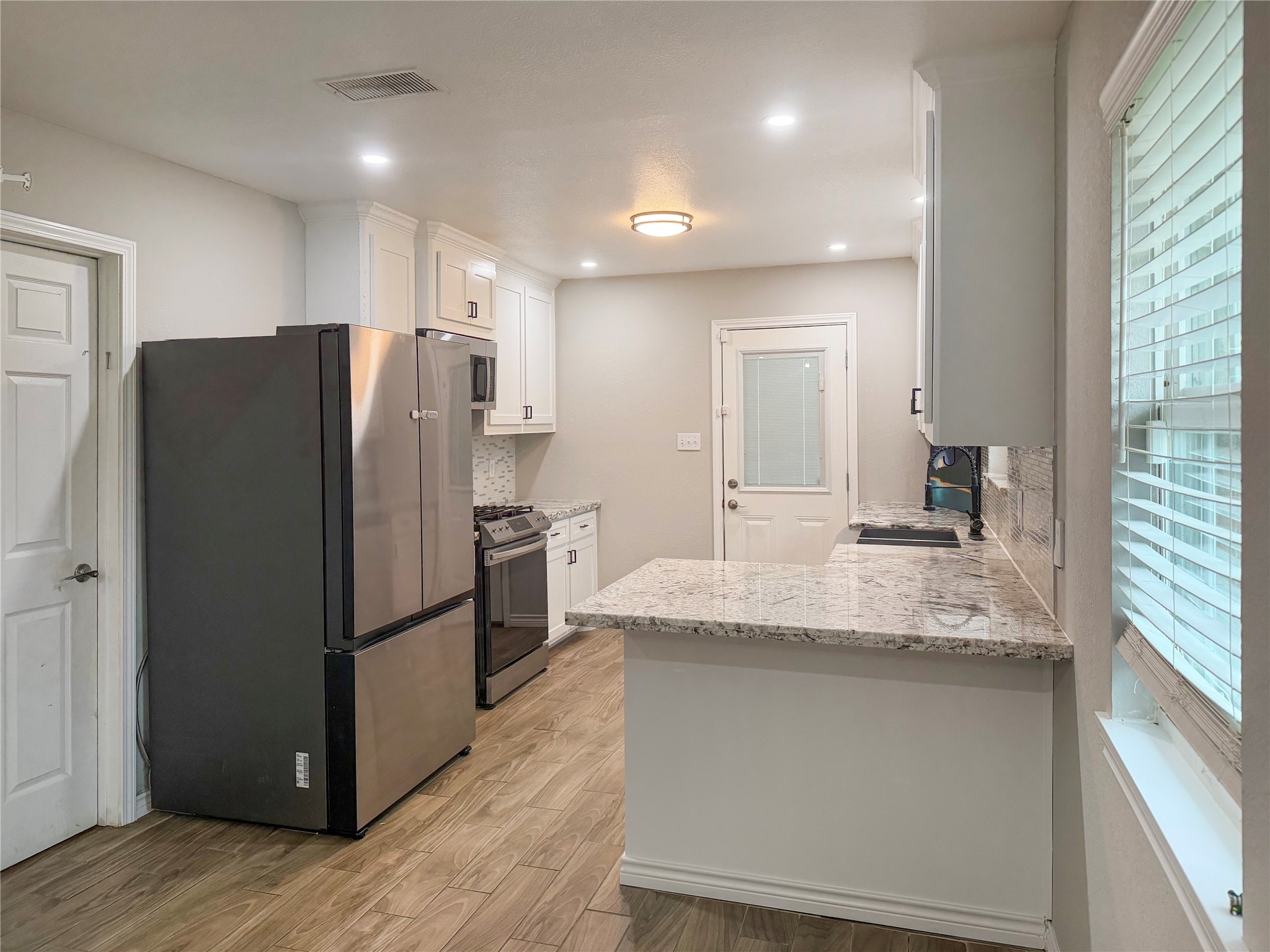 Kitchen features white cabinetry, a stainless steel sink, and a window overlooking the backyard, bringing in natural light and offering pleasant outdoor views.