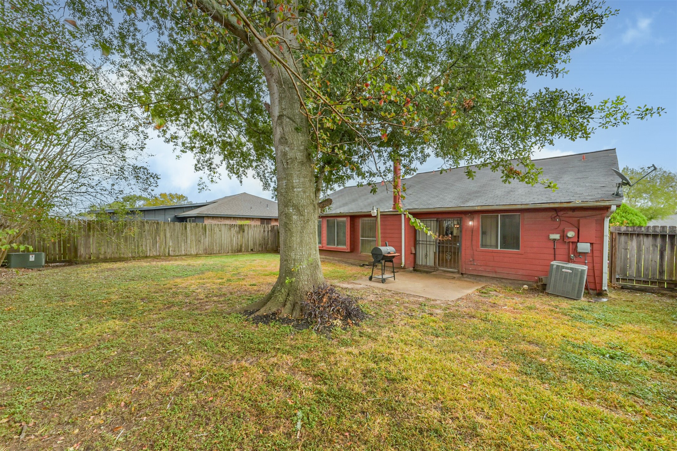 Spacious backyard with a large tree providing shade, a patio perfect for outdoor dining, and a wooden fence for privacy.