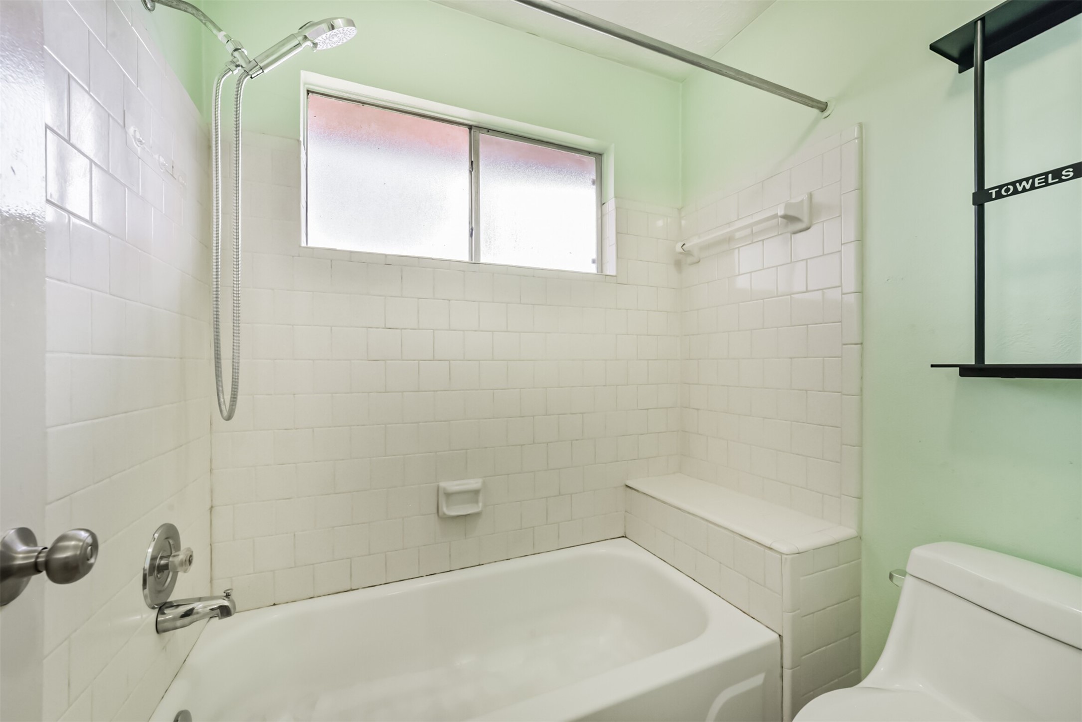 Bright and airy bathroom featuring classic white tiles, a built-in bathtub, and a convenient showerhead, complemented by natural light from the frosted window.