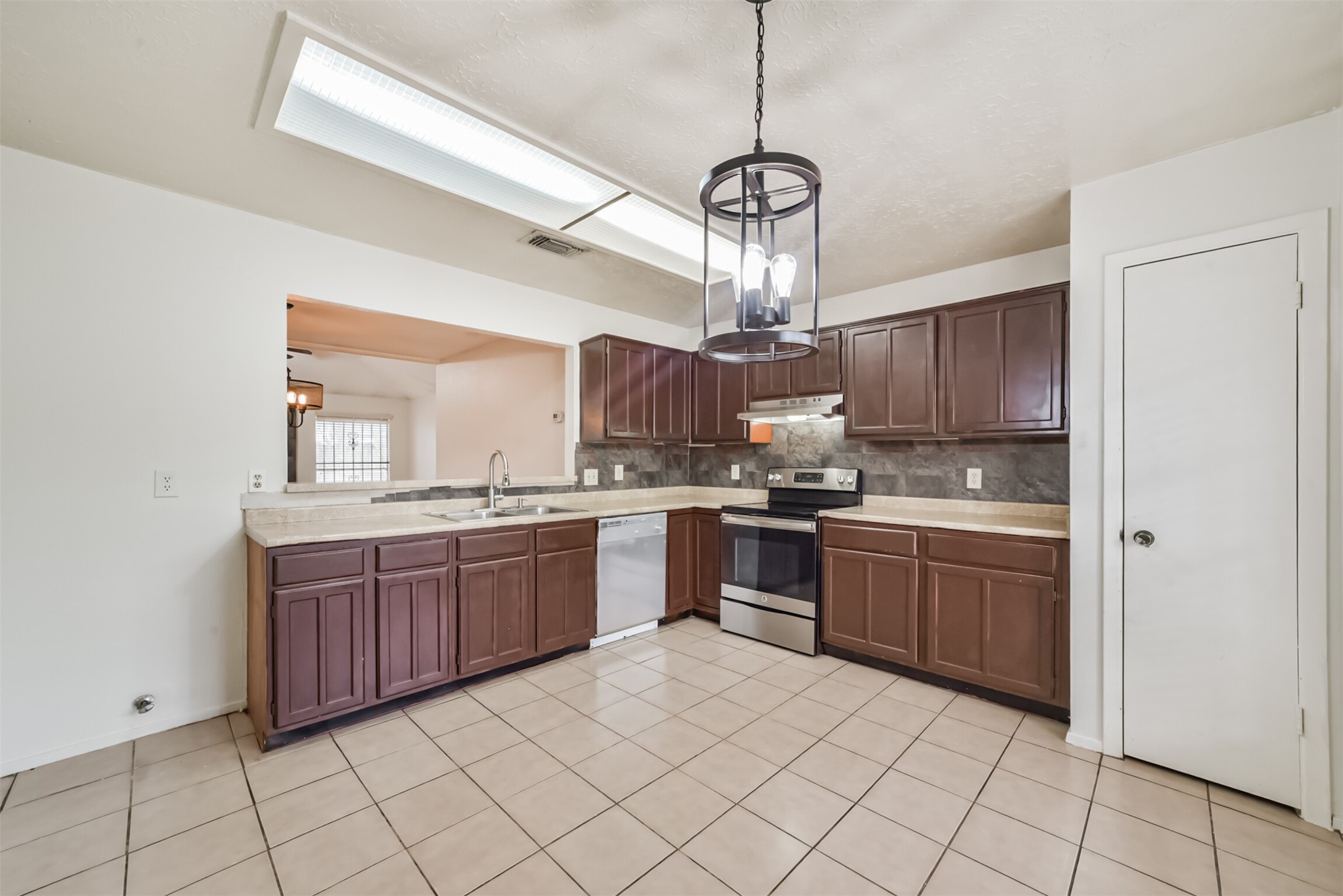 Spacious kitchen featuring dark wood cabinetry, modern stainless steel appliances, and ample counter space, accented by a stylish overhead light fixture.