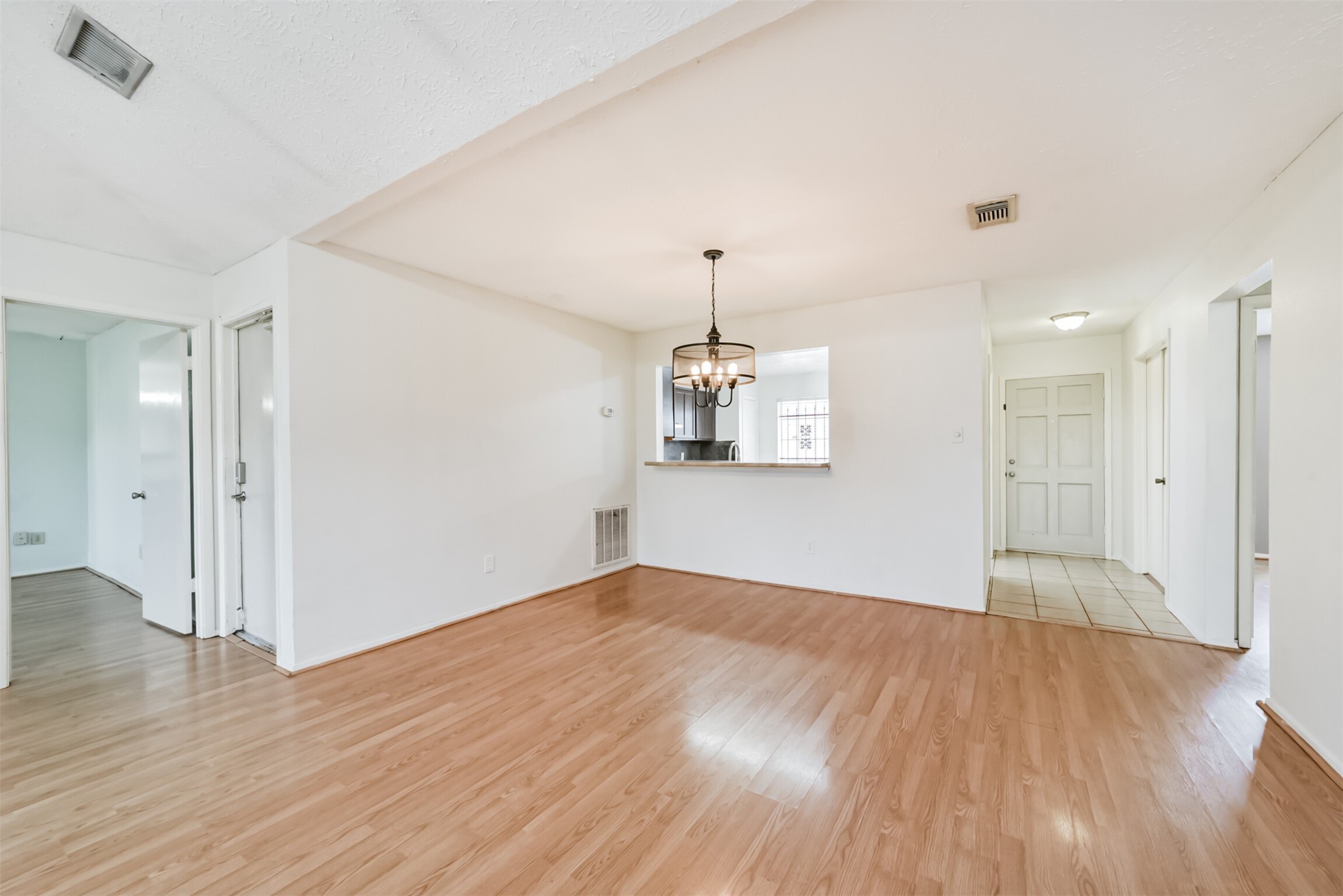 Spacious, light-filled living area with wood flooring, an elegant chandelier, and an open layout leading to the kitchen, creating a welcoming atmosphere.