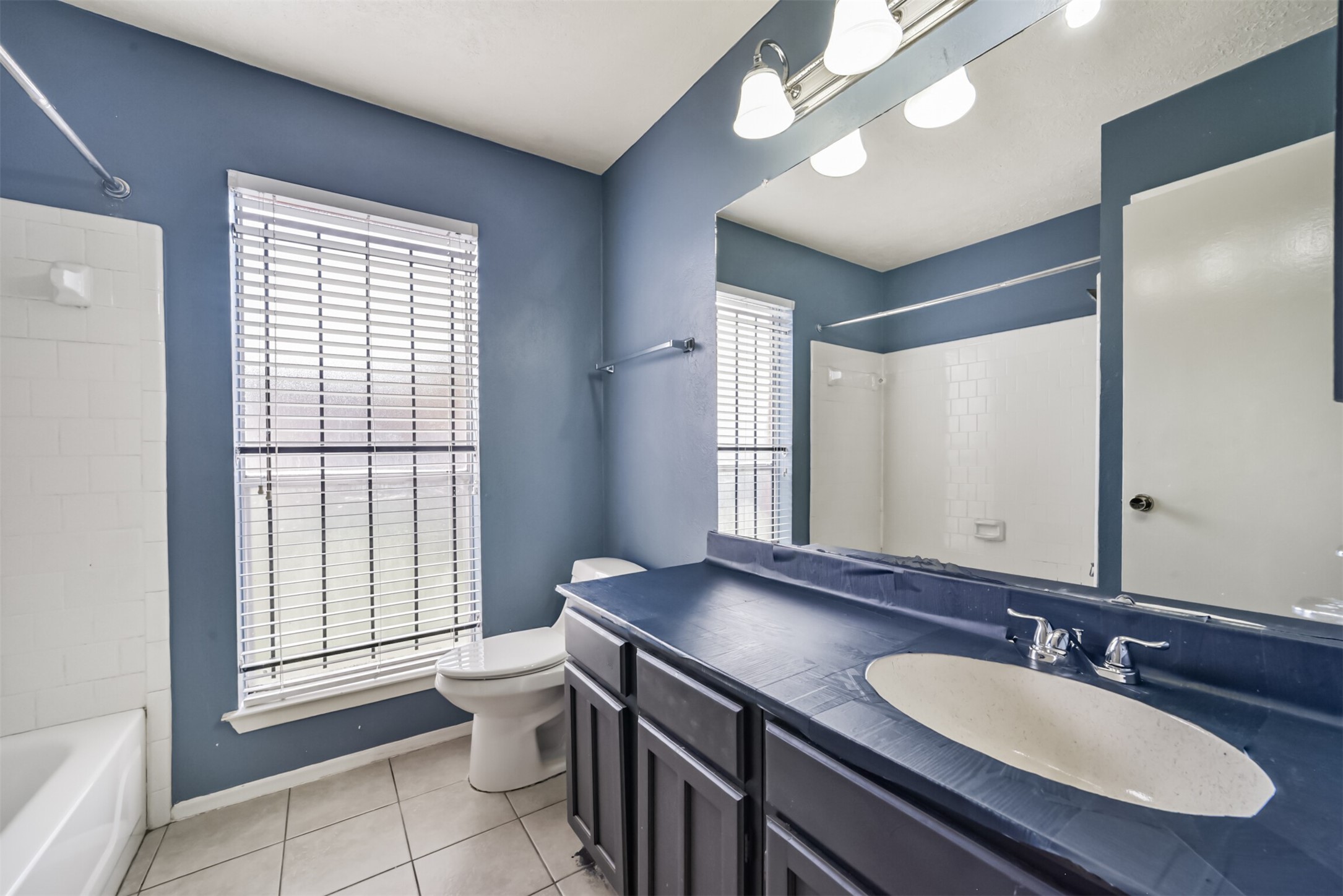 Charming bathroom with a spacious vanity, elegant blue walls, and abundant natural light from a large window, complemented by a classic white tub and modern fixtures.