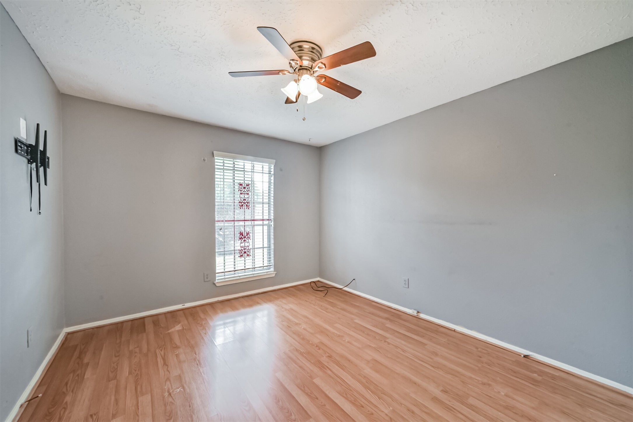 Bright room with hardwood floors, neutral gray walls, and a ceiling fan, perfect for a cozy retreat or home office.