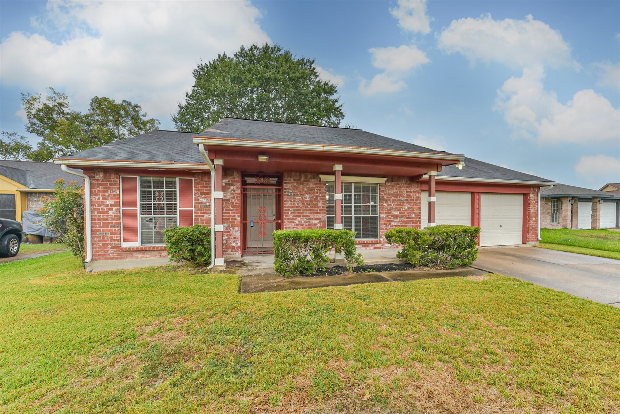 Charming brick home with a welcoming front porch, lush green lawn, and 2 car garage.