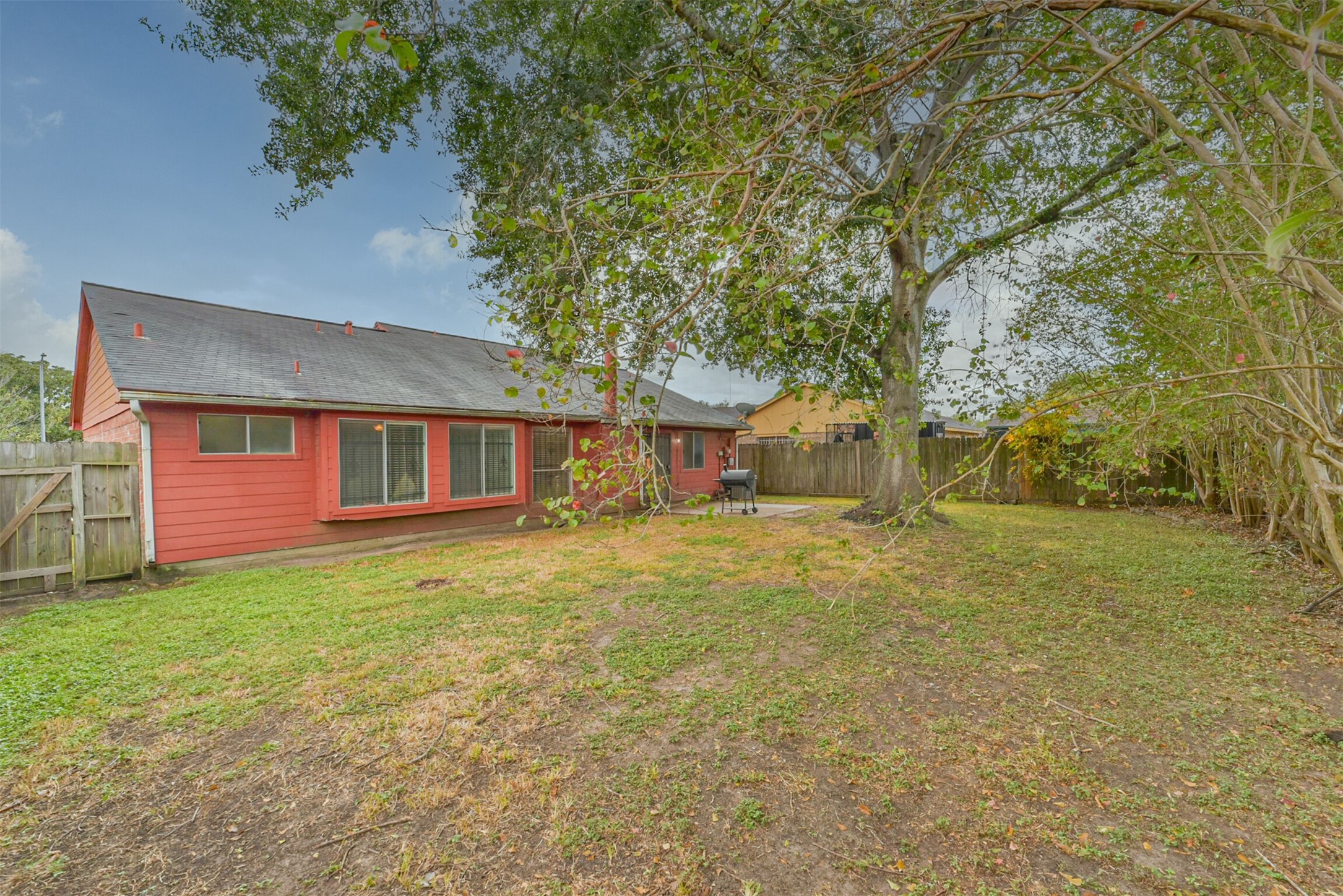 Spacious backyard featuring a charming red house with ample lawn space, mature trees for shade, and a cozy patio area perfect for outdoor gatherings.