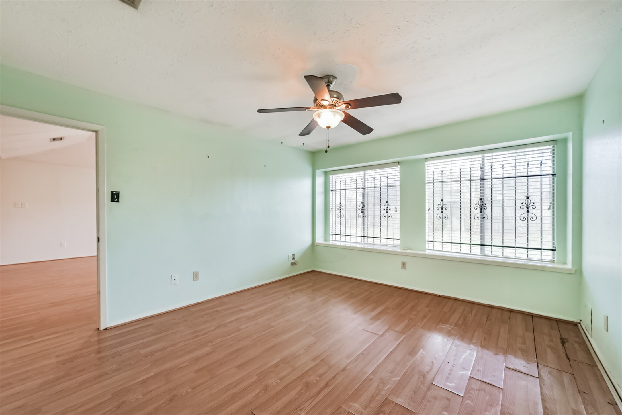 Bright room with large windows featuring decorative ironwork, sleek laminate flooring, and a ceiling fan for added comfort and style.