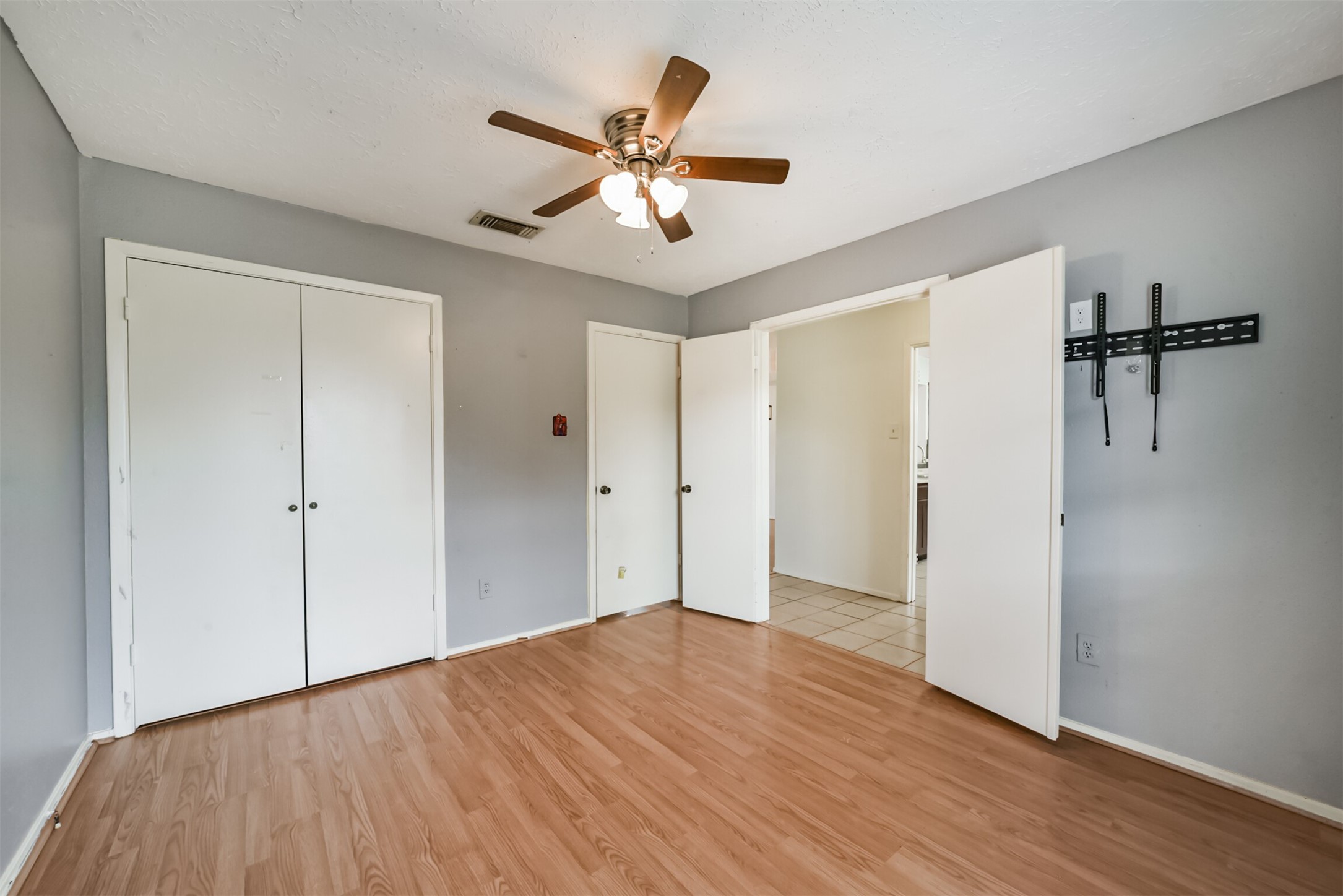 Spacious bedroom featuring laminate wood flooring, a ceiling fan, and ample closet space with dual white doors, offering a bright and airy feel.