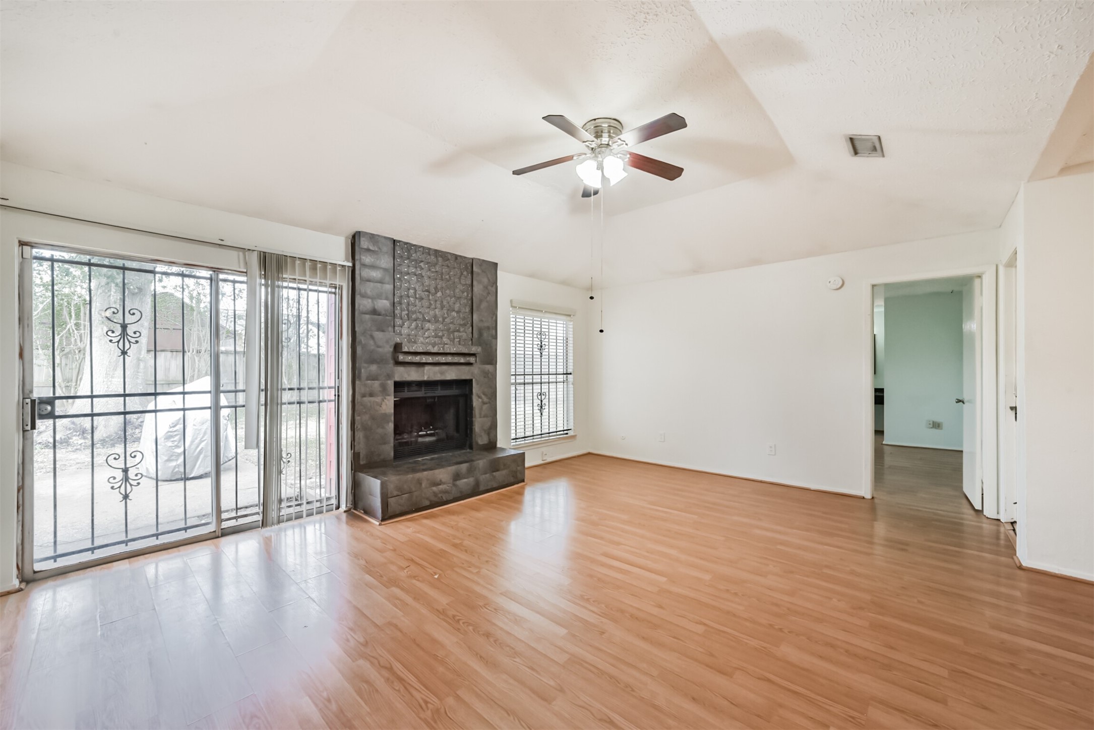 Spacious living room featuring laminate wood flooring, a cozy fireplace, and abundant natural light from large windows and sliding glass doors leading to the patio.