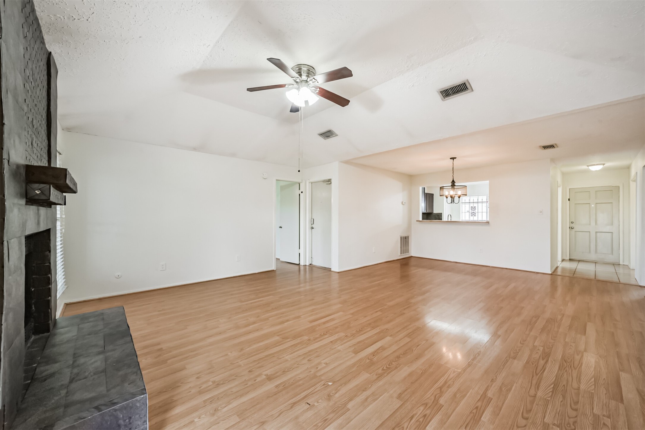 Spacious living area featuring elegant hardwood floors, a cozy fireplace, and an open layout with a ceiling fan for comfort.