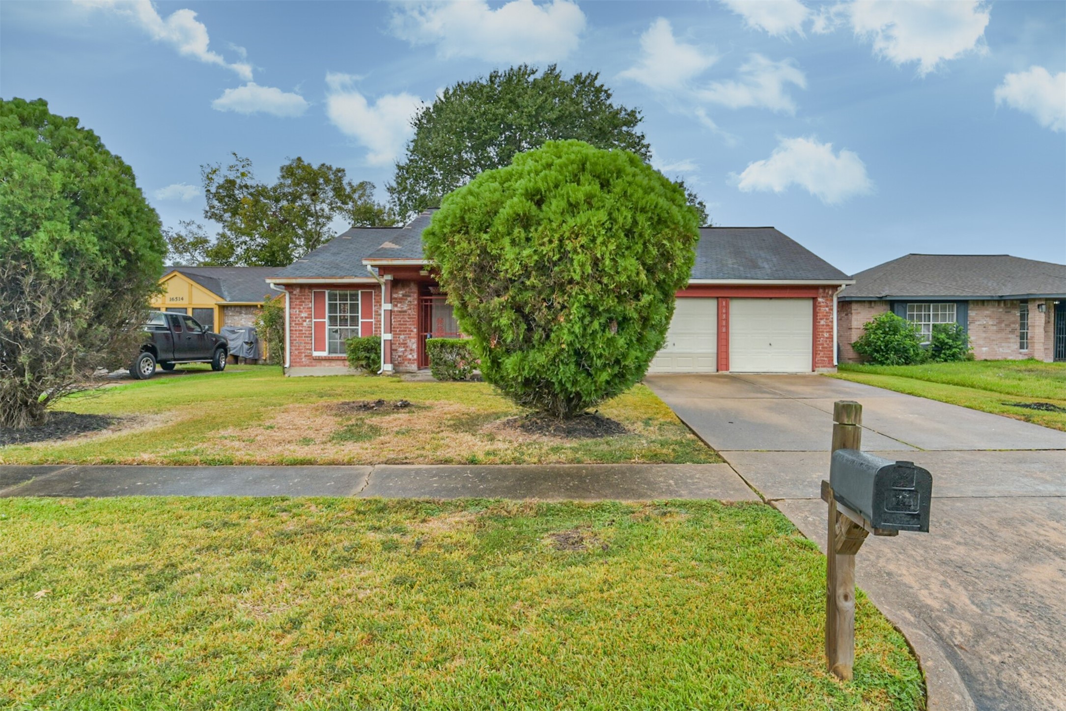 One story brick home with a welcoming front porch, two-car garage, and lush greenery.