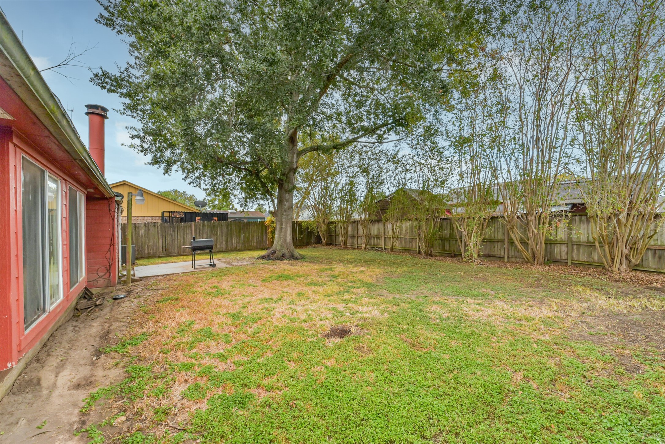 Expansive backyard with lush greenery, mature trees, and a cozy patio perfect for outdoor grilling and relaxation.