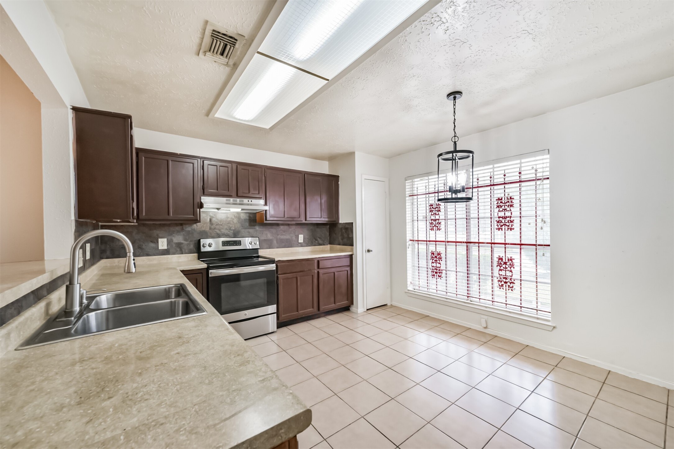 Spacious kitchen with modern stainless steel appliances, rich wooden cabinetry, and ample counter space, complemented by a bright dining area with large windows and elegant tile flooring.