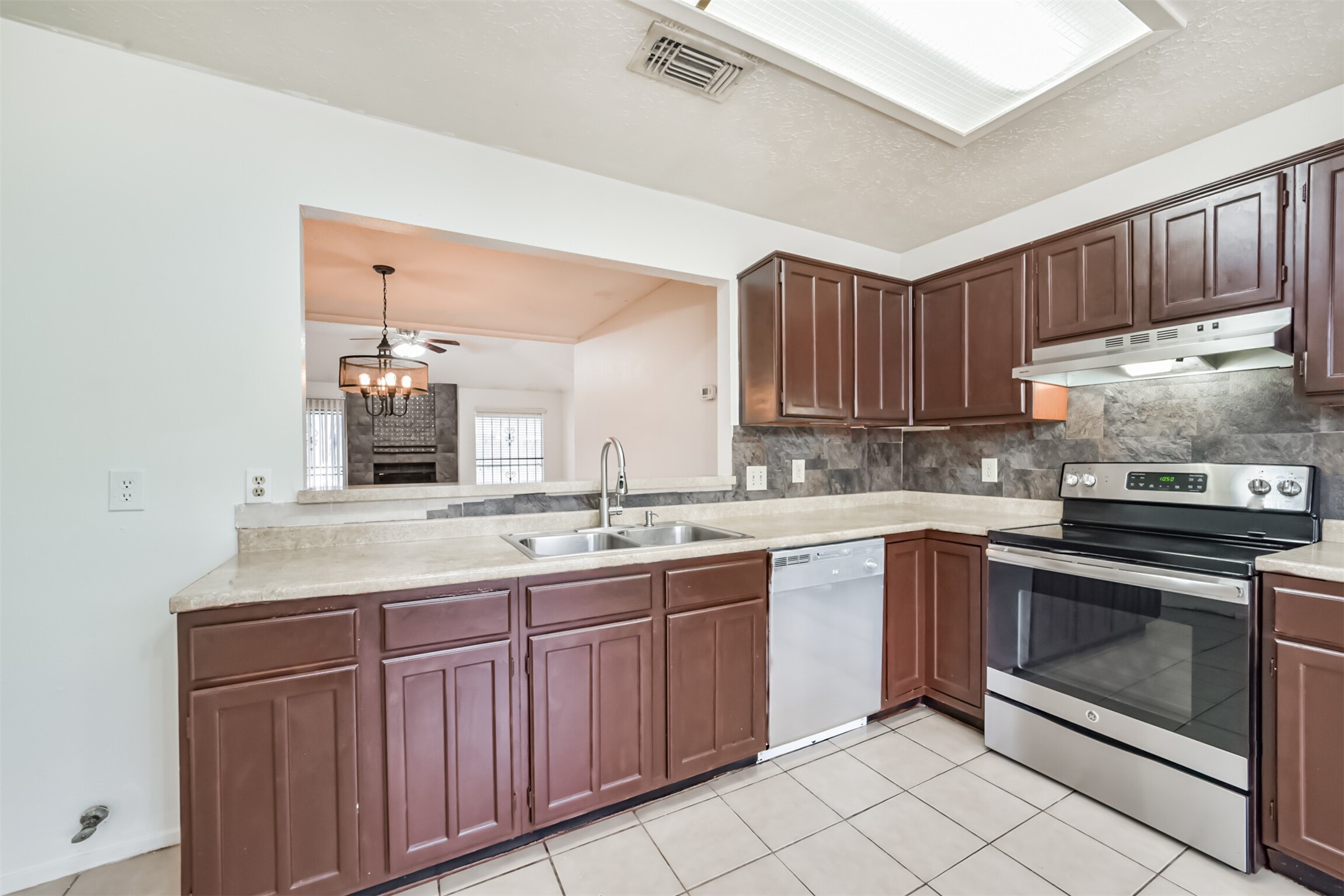 Charming kitchen with rich wood cabinetry, modern stainless steel appliances, and a convenient pass-through window to the cozy living area featuring a fireplace.