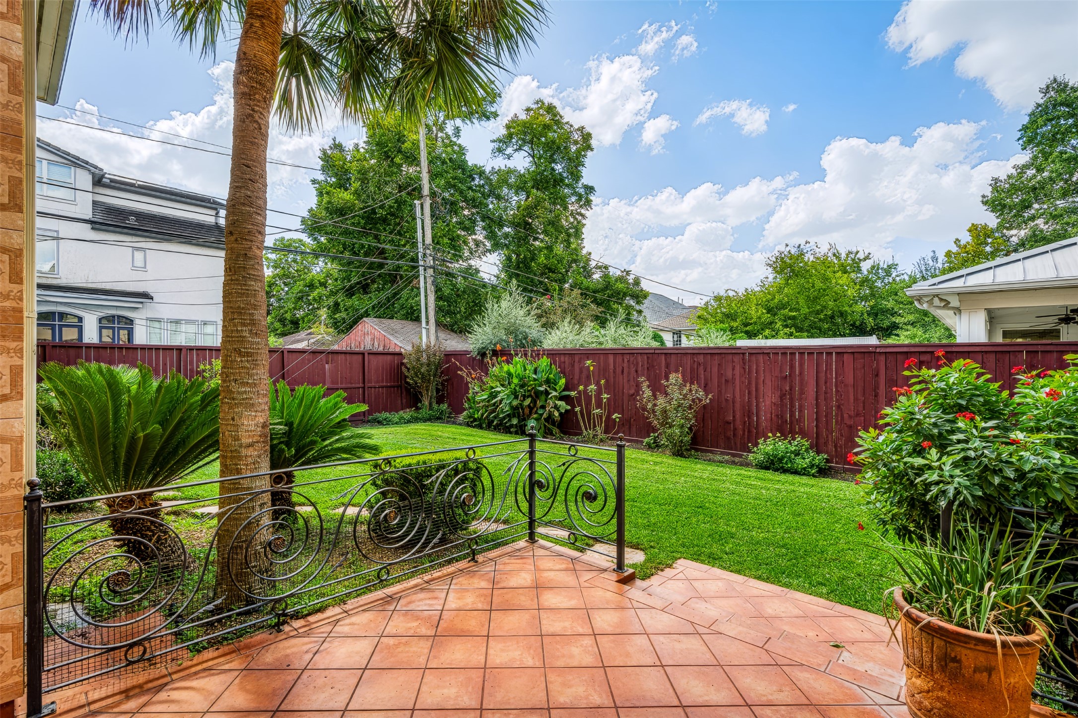 Charming backyard oasis with a tiled patio, lush greenery, and vibrant landscaping, perfect for relaxation and entertaining.