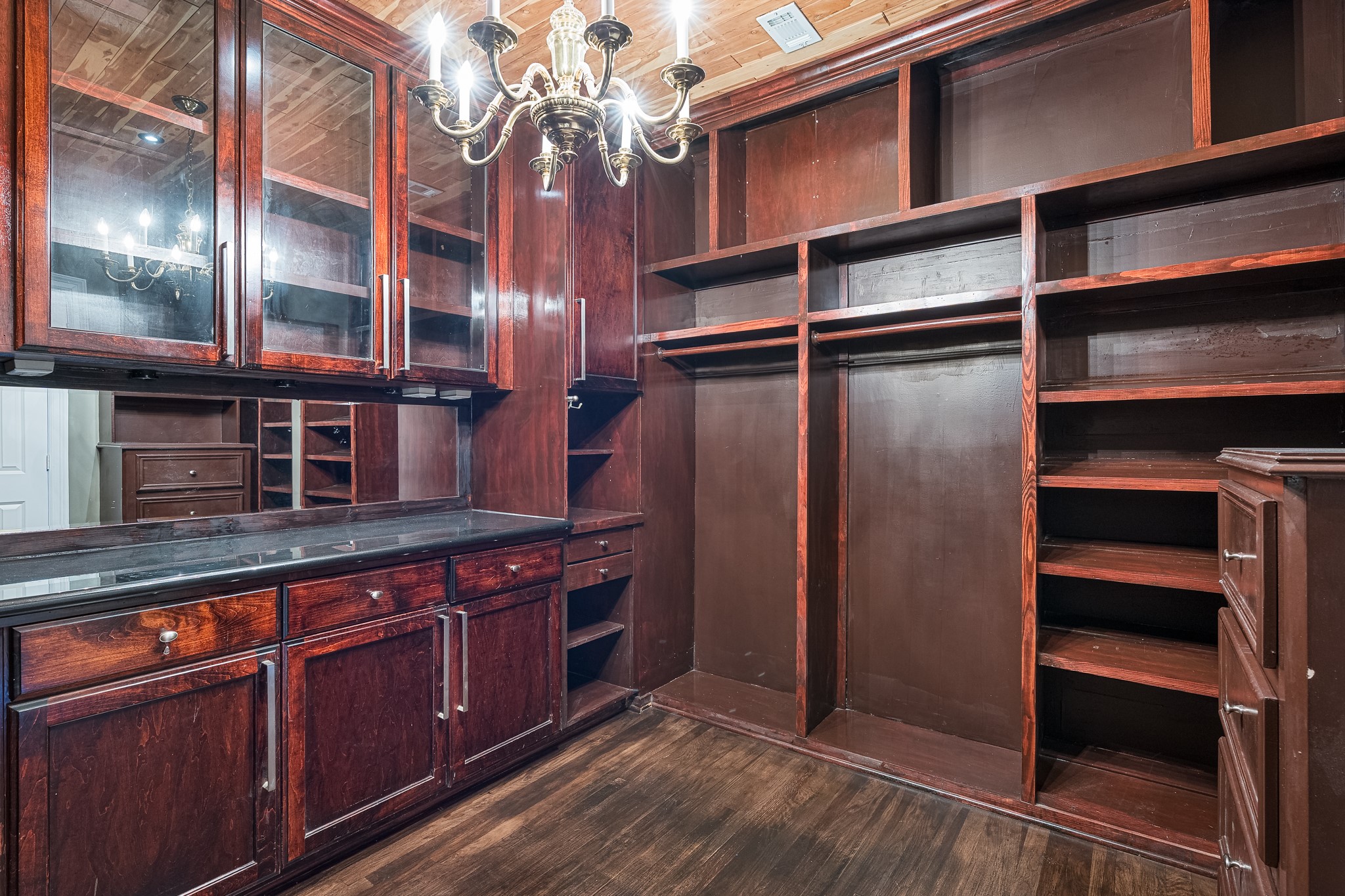 Second luxurious walk-in primary closet featuring rich wood cabinetry, ample shelving, and a classic chandelier, perfect for organizing and displaying your wardrobe in style.
