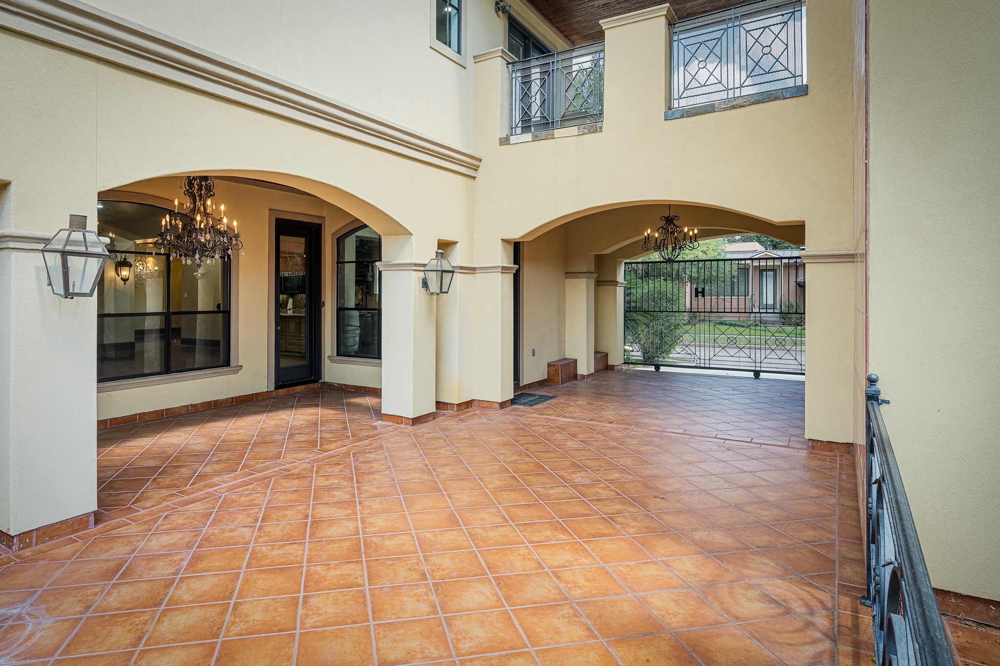Elegant covered patio with terracotta tile flooring, graceful arches, and stylish chandeliers, offering a sophisticated outdoor living space. Automatic gate opens to the driveway if needed