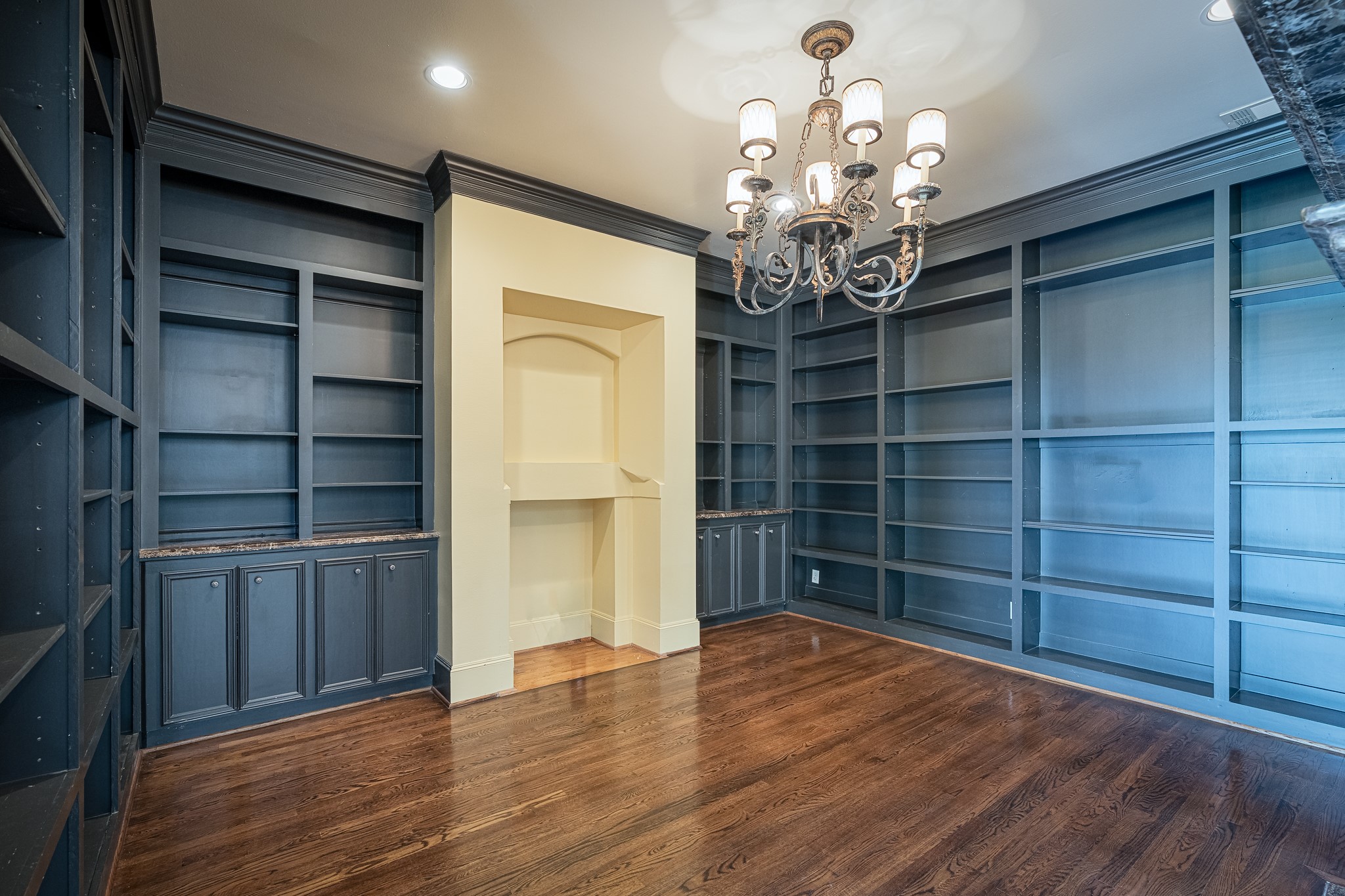 Elegant study featuring rich hardwood floors, built-in shelving, and a sophisticated chandelier, perfect for a home office or library.