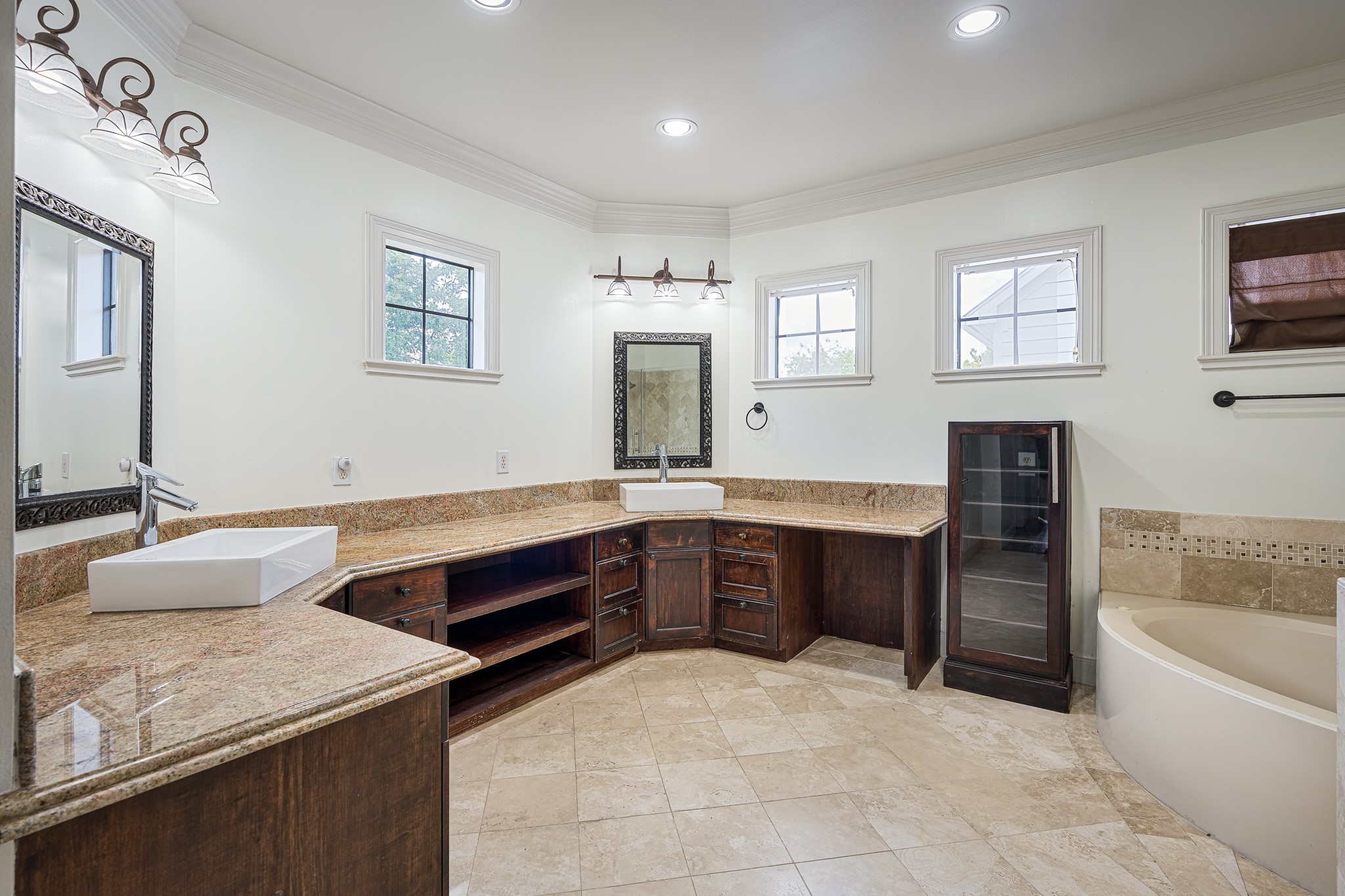 Spacious bathroom featuring elegant granite countertops, dual sinks, and a luxurious soaking tub, complemented by rich wooden cabinetry and natural light from multiple windows.