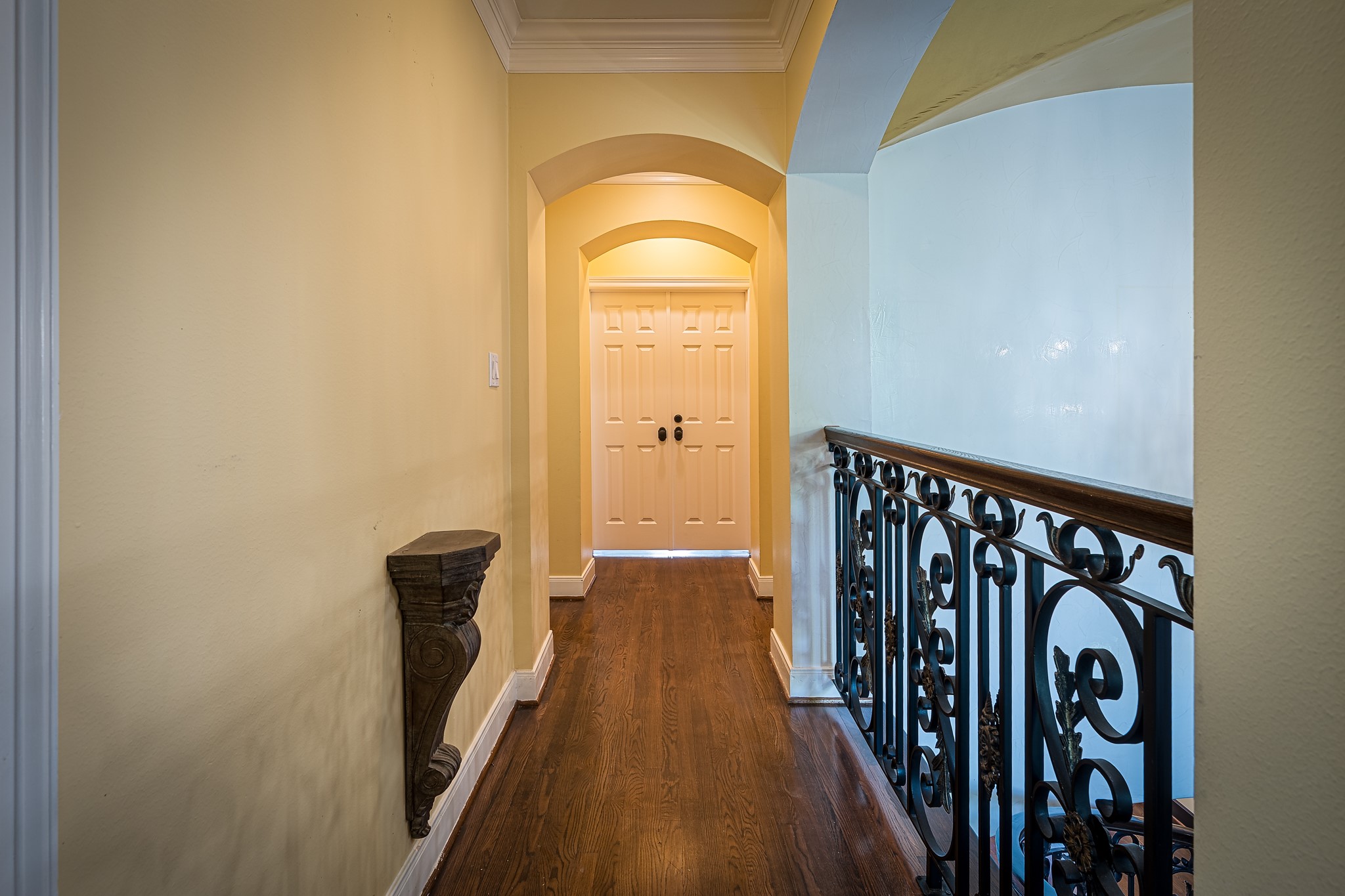 Elegant hallway with rich hardwood floors, featuring a decorative wrought iron railing and soft yellow walls, leading to the Primary Bedroom.