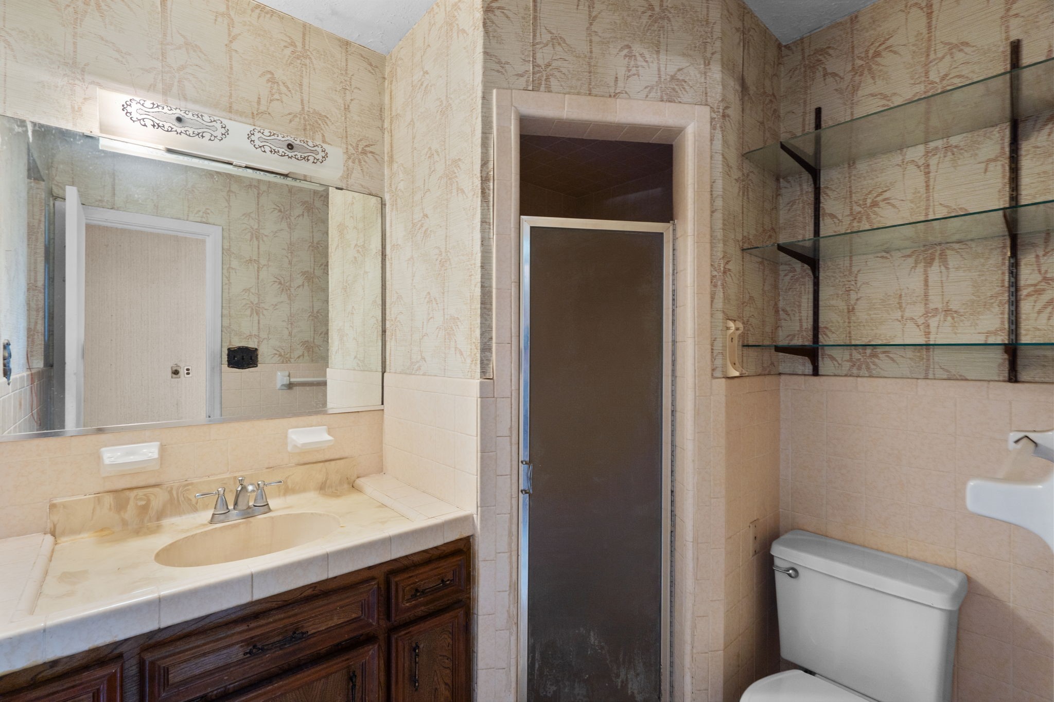 Bathroom with tiled shower, vanity, and glass shelving.