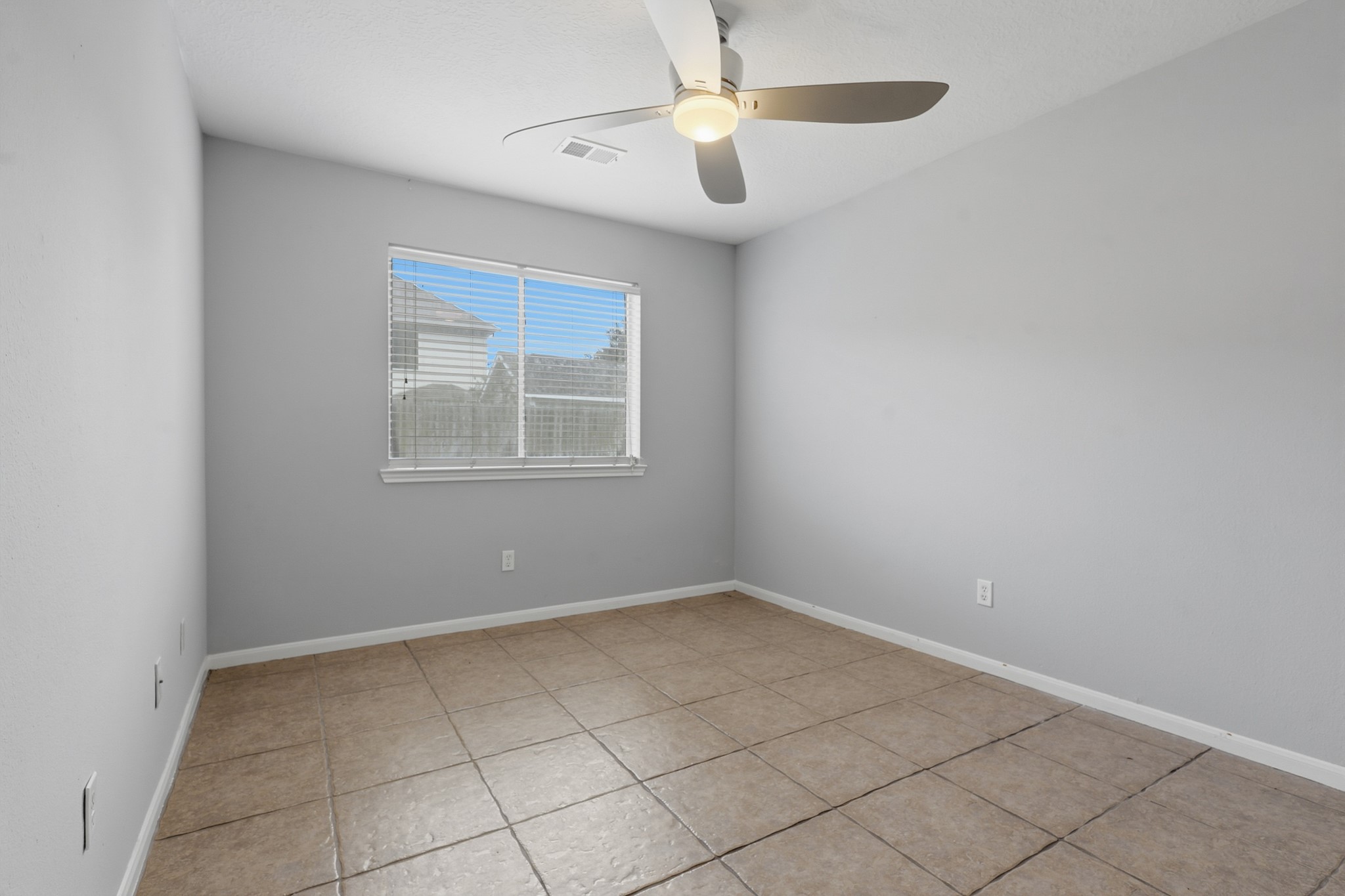 Versatile secondary bedroom with tile flooring, ceiling fan and neutral finishes.