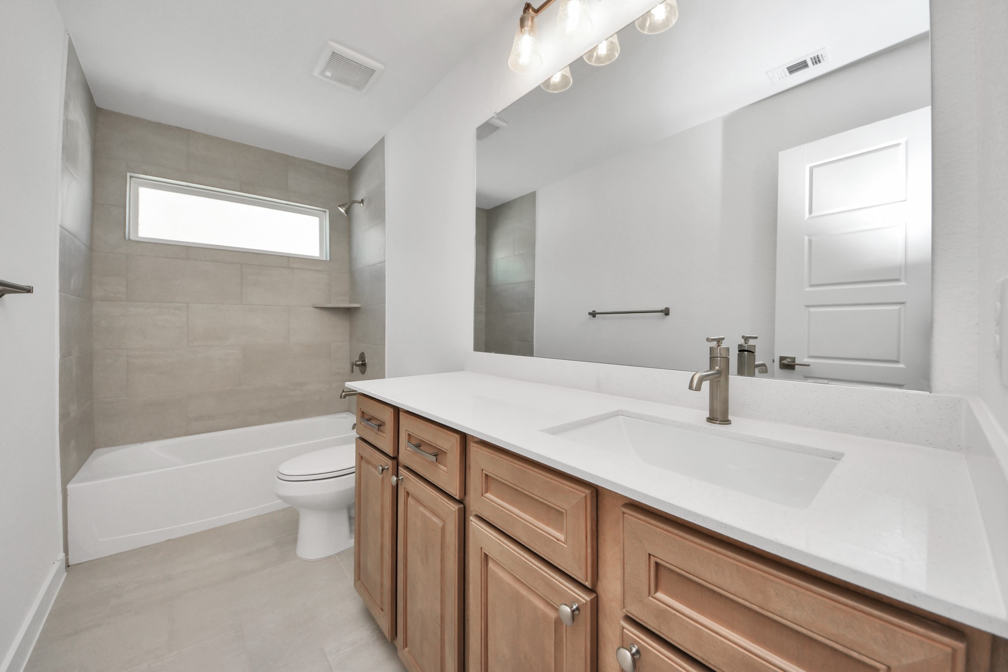 Secondary bath features tile flooring, bath/shower combo with tile surround, light stained wood cabinets, beautiful light countertop.