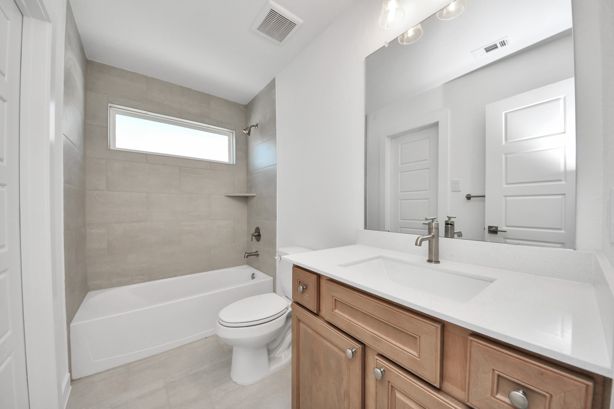 Secondary bath features tile flooring, bath/shower combo with tile surround, light stained wood cabinets, beautiful light countertop.