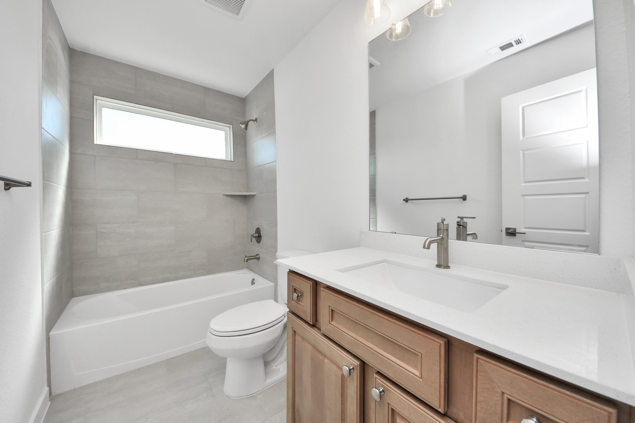 Secondary bath features tile flooring, bath/shower combo with tile surround, light stained wood cabinets, beautiful light countertop.