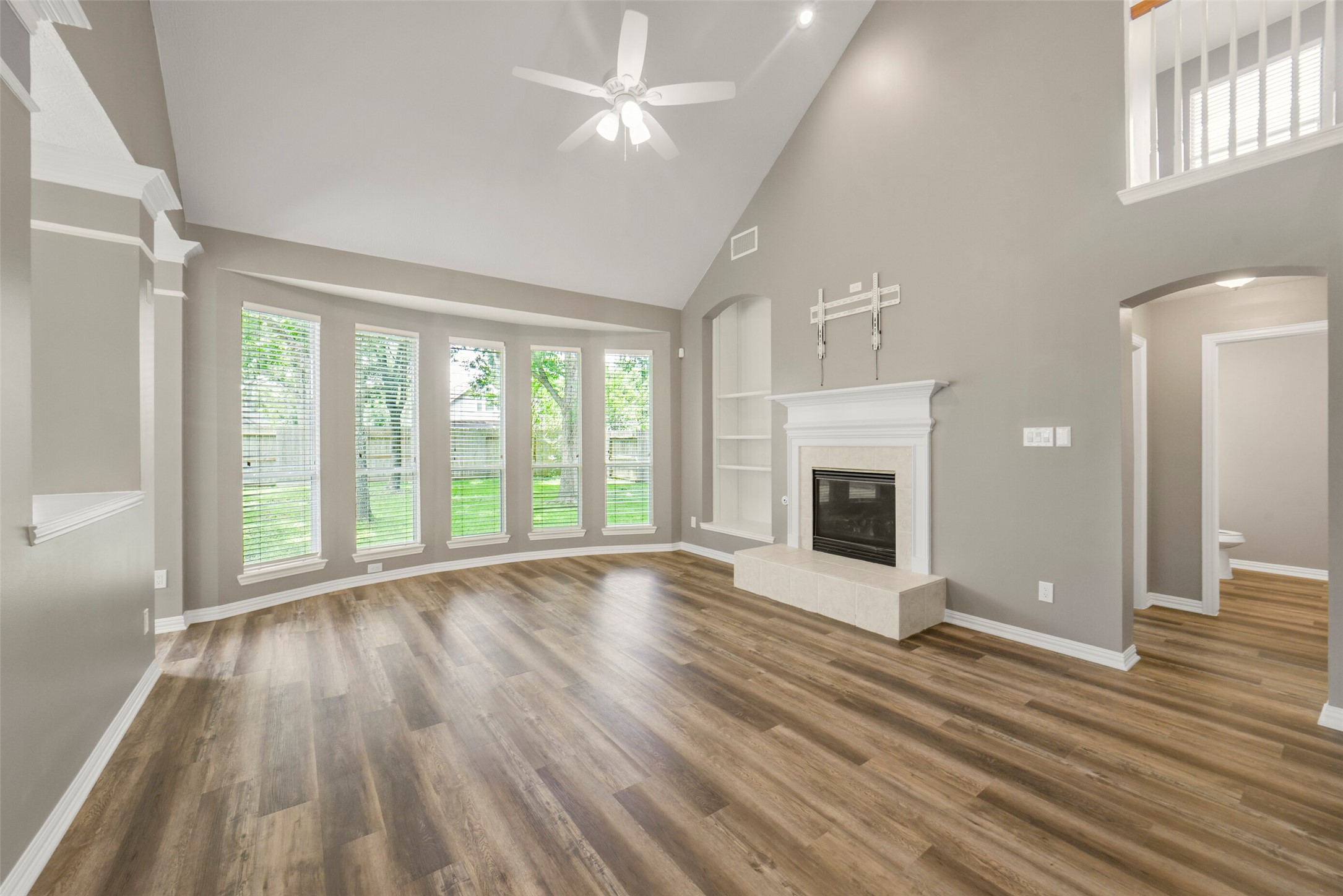 The breathtaking living room boasts built-in shelving, a fireplace, soaring high ceilings, and massive windows that flood the space with natural light.