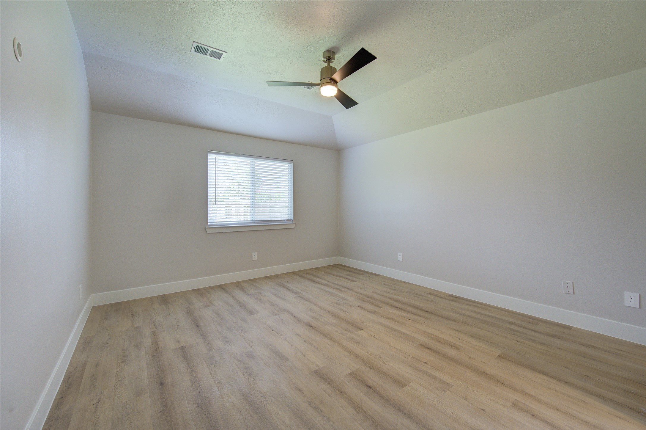 The spacious primary bedroom features a vaulted ceiling, modern ceiling fan, updated wood-look flooring and a large window to fill the room with natural light