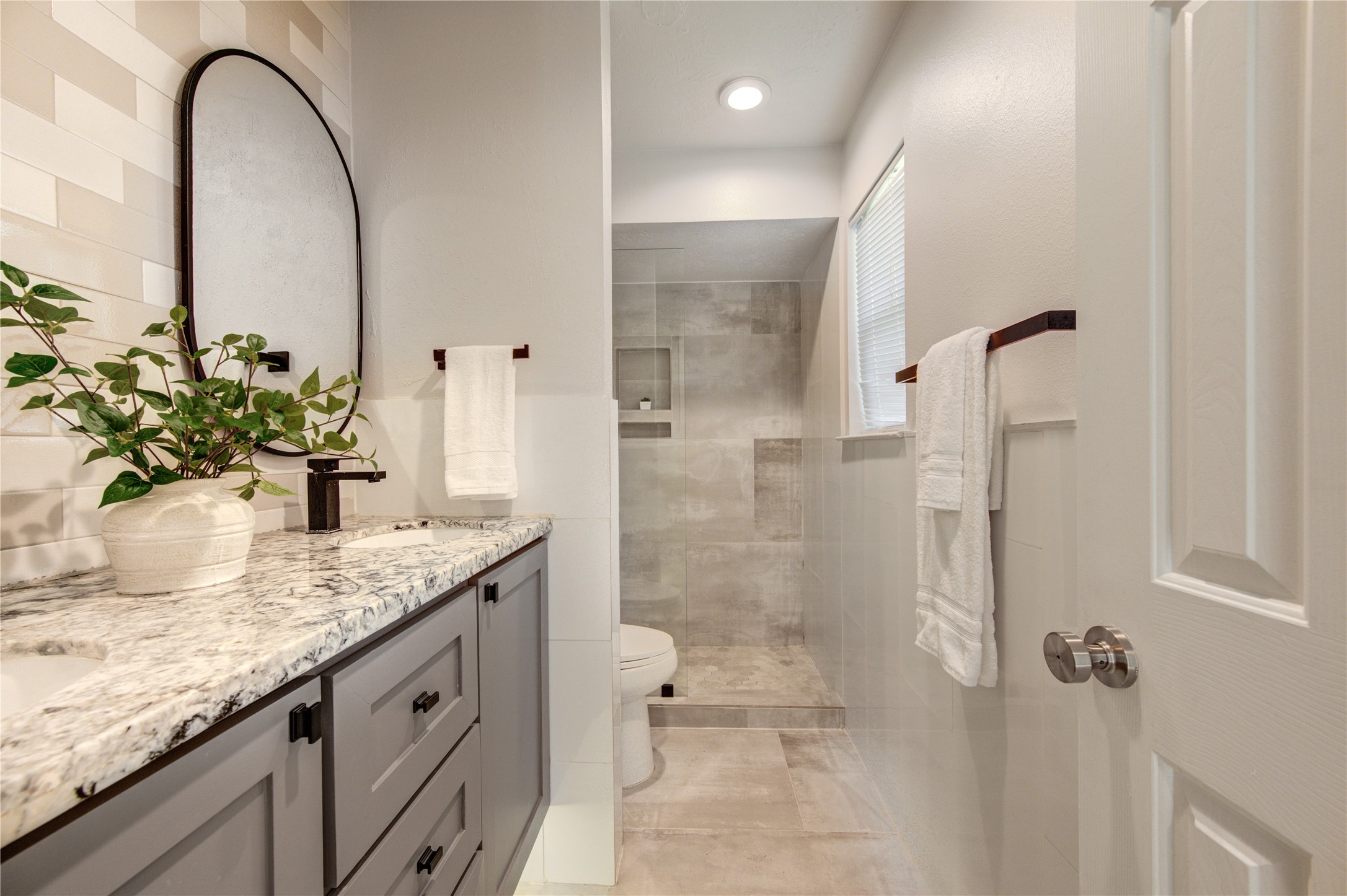 stylish bathroom featuring a granite-topped vanity, contemporary black fixtures and a spacious walk-in shower with elegant tilework